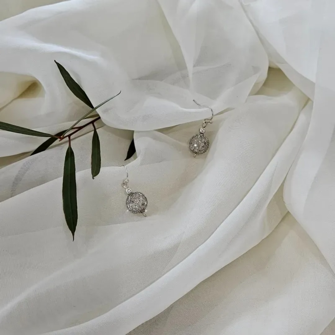 White fabric with small silver earrings and a sprig of green leaves