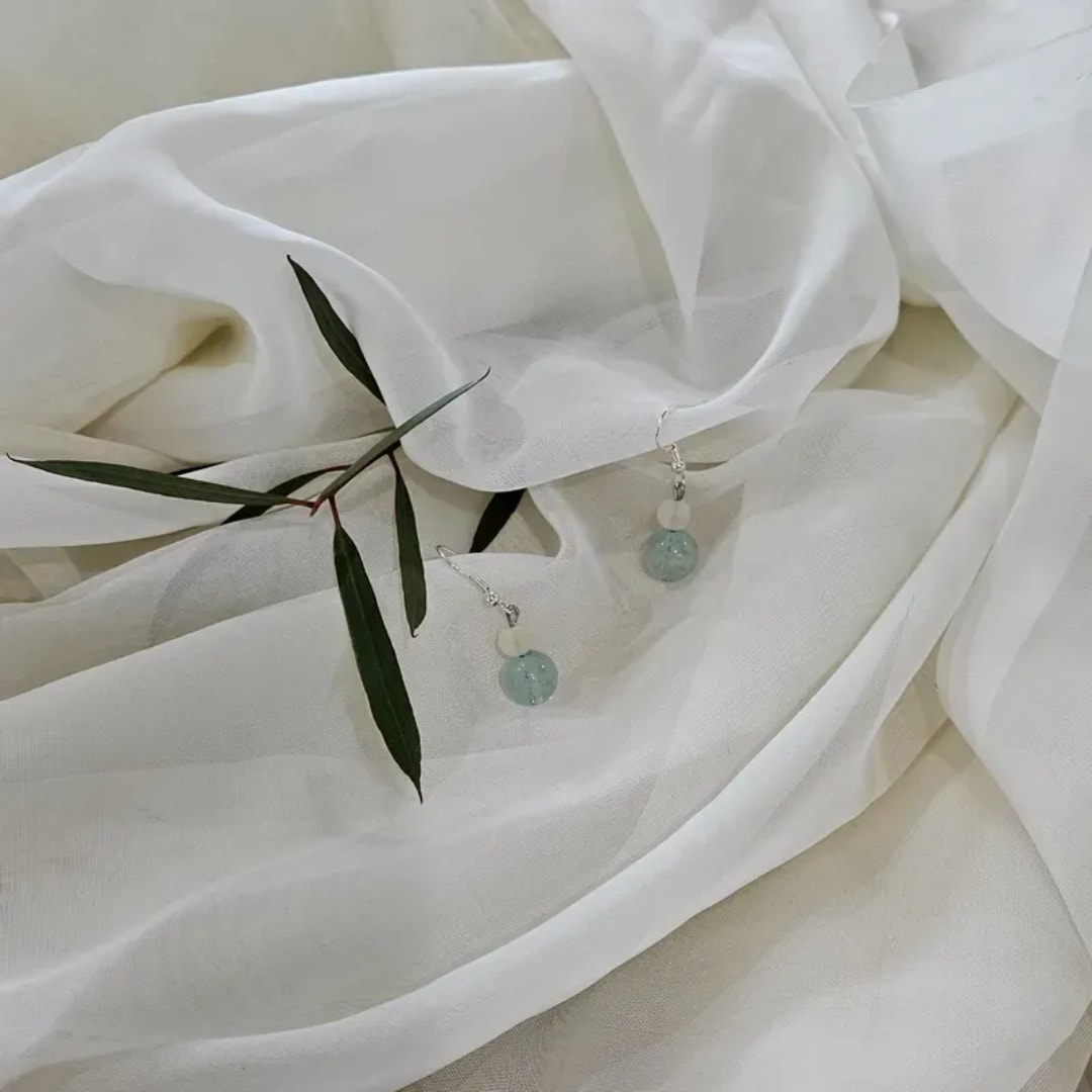 White fabric with two dangling blue bead earrings and a few green leaves