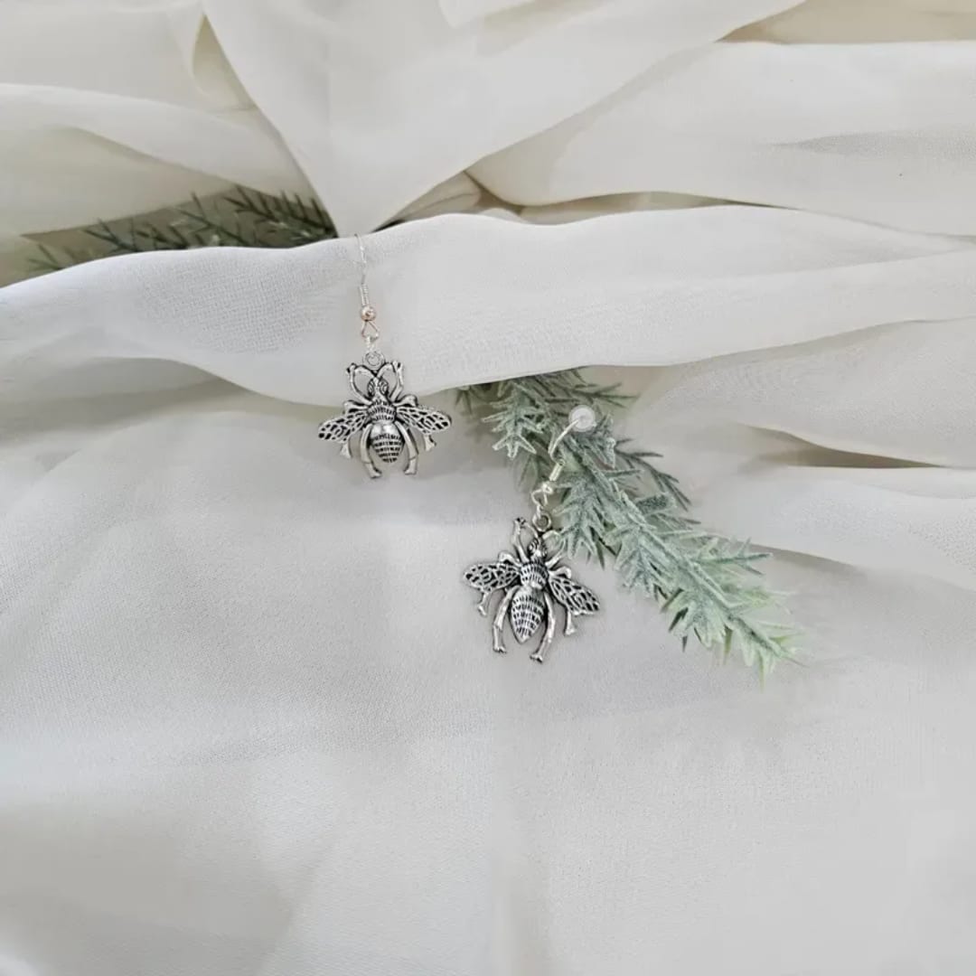 Bee-shaped earrings on white fabric with faux greenery