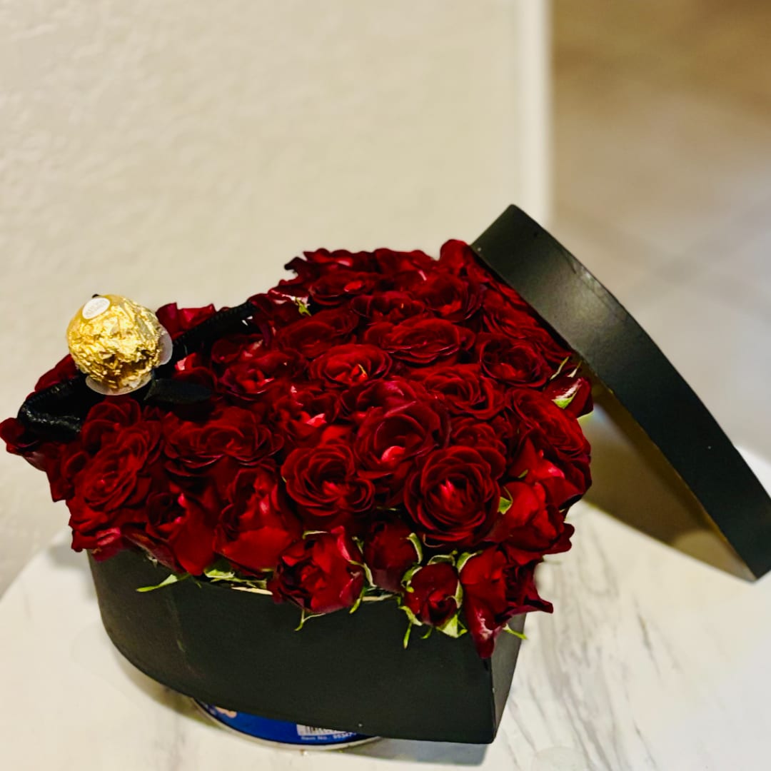 Red roses arranged in a black box with a gold-wrapped chocolate