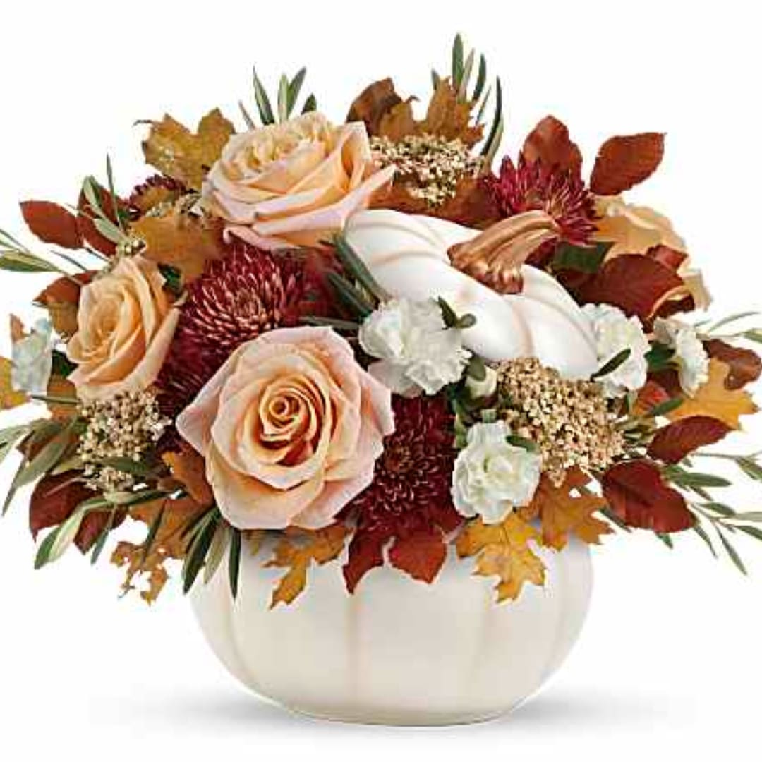 Peach roses and white flowers in a white pumpkin vase with autumn leaves