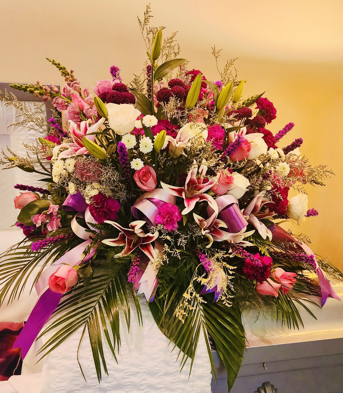 Large pink and white floral spray with ribbons on a casket
