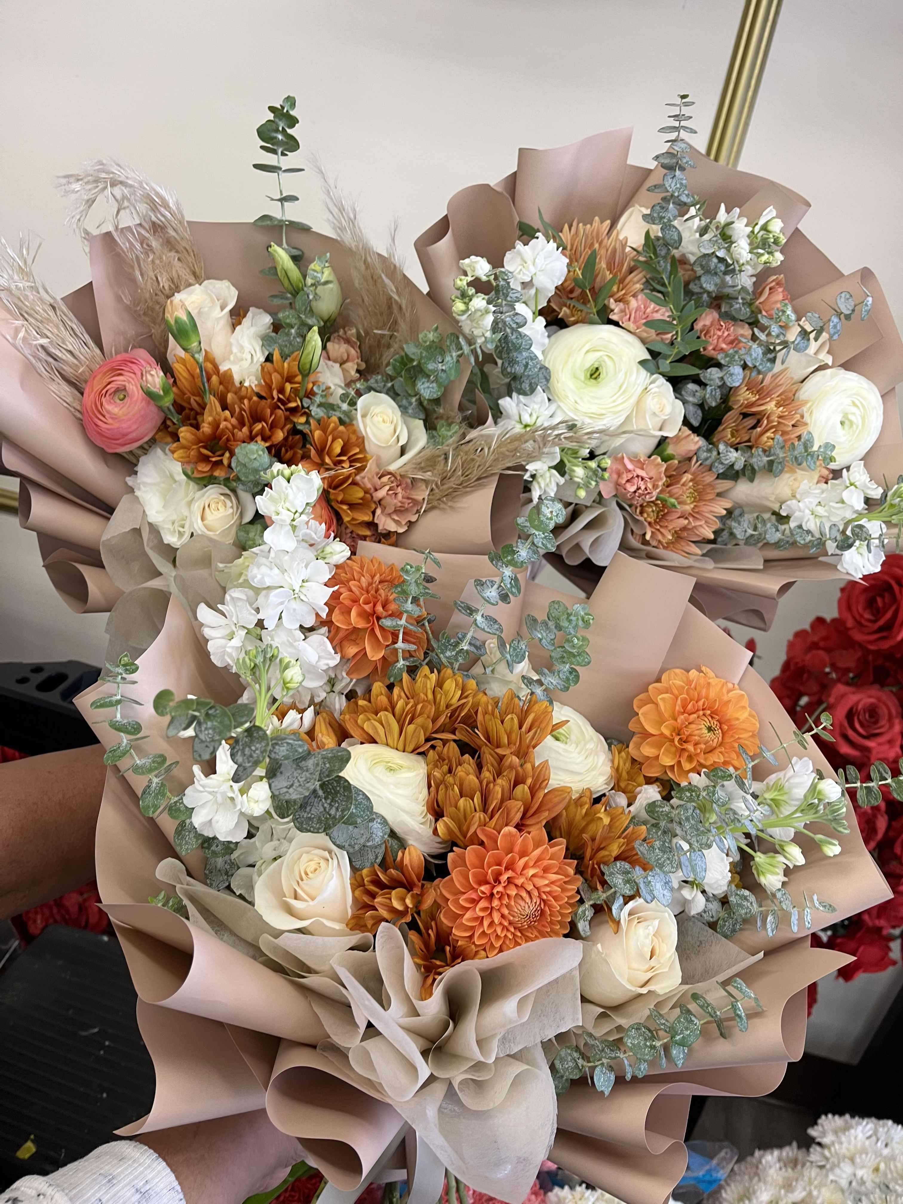 Three wrapped bouquets with orange, white, and cream flowers