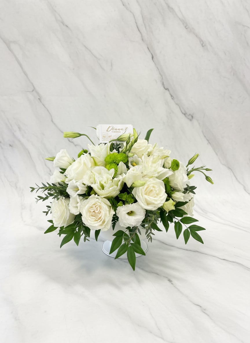 White floral arrangement in a low vase with green accents