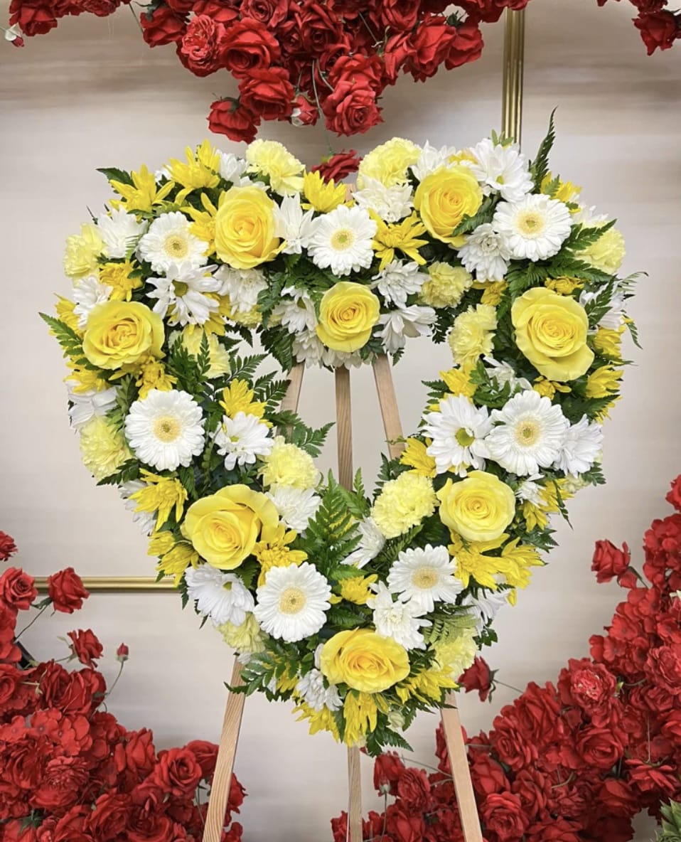 Heart-shaped floral wreath with yellow roses and white daisies on an easel