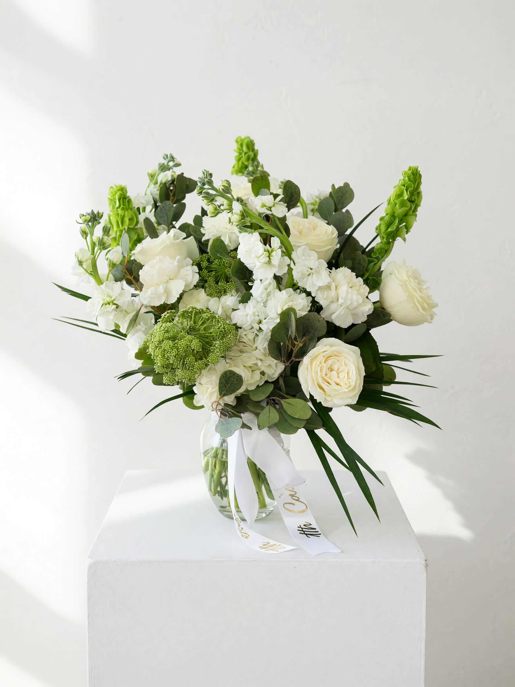 White and green bouquet in a clear glass vase with a ribbon