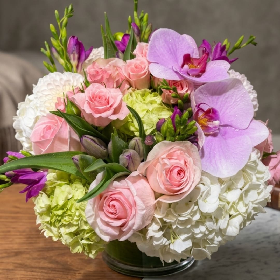 Pink roses and purple orchids arranged with white hydrangeas in a glass vase