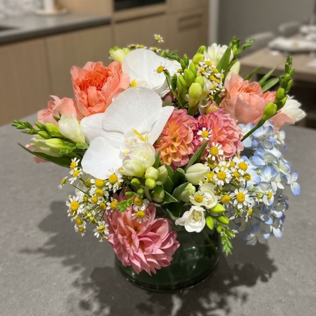 Mixed bouquet of white orchids, peach and pink blooms in a glass vase