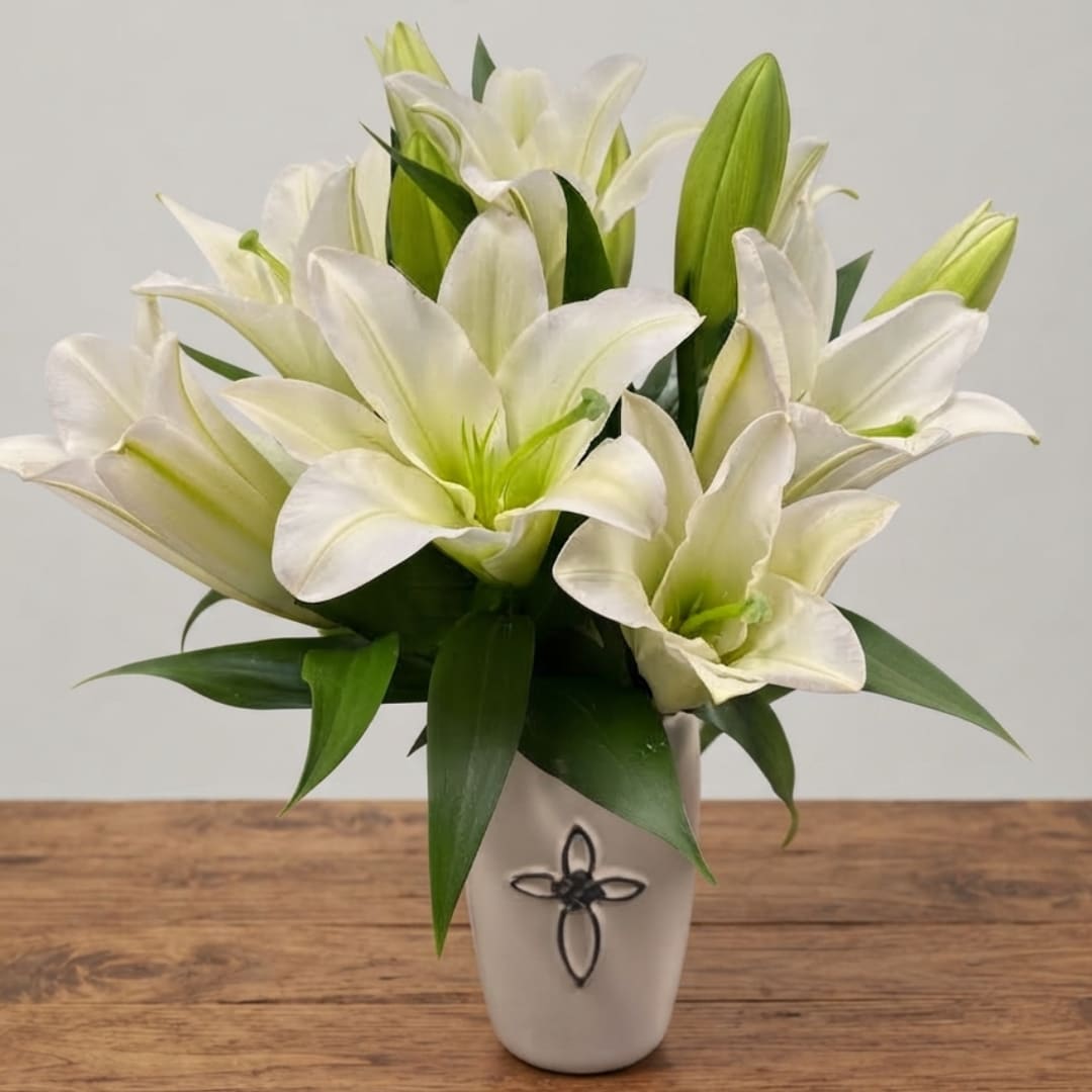 White lilies arranged in a white vase on a wooden table