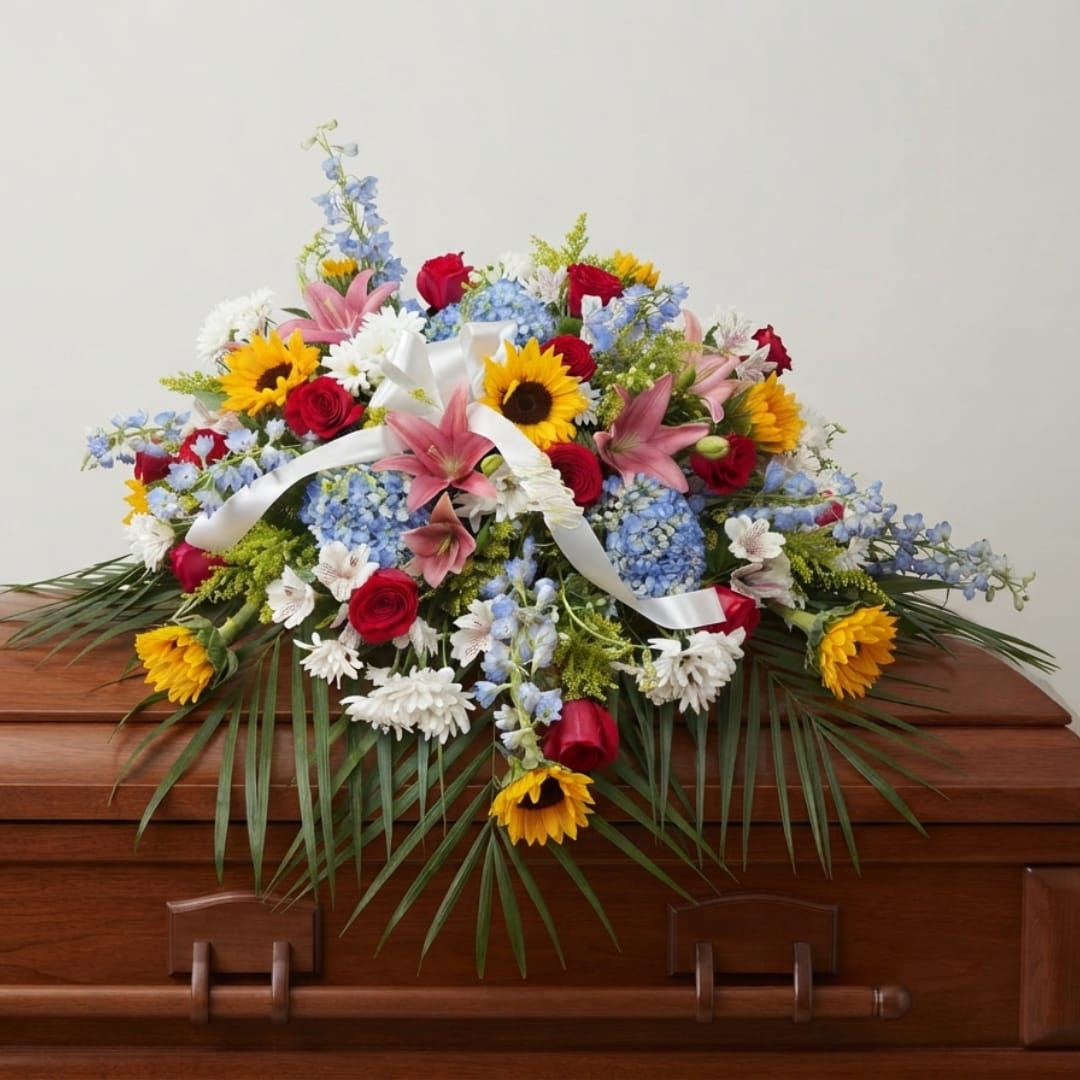 Colorful floral casket spray with lilies, roses, sunflowers, and blue blooms