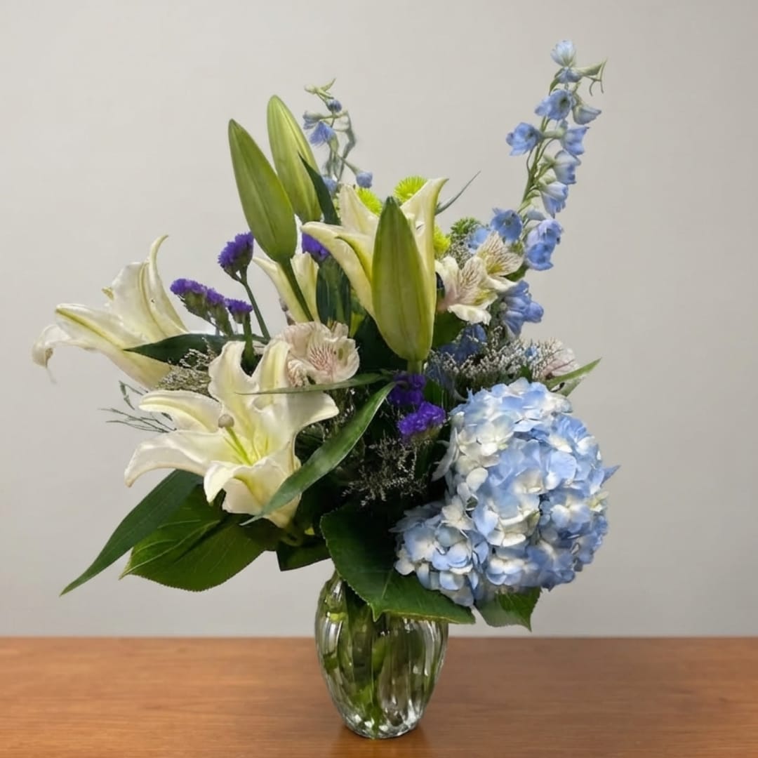 Blue hydrangea and white lily arrangement in a clear glass vase
