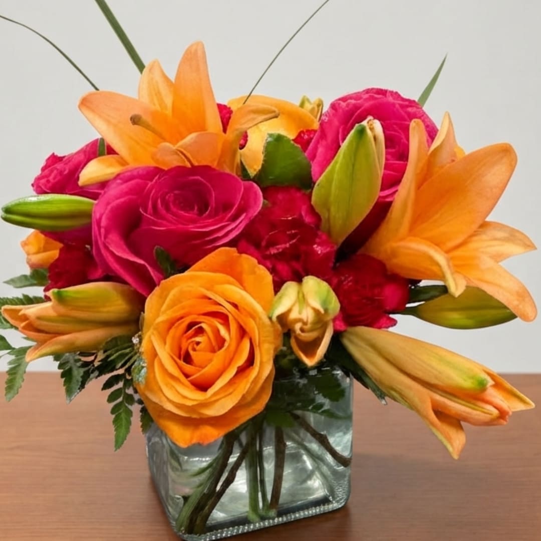Orange lilies and pink roses arranged in a square glass vase