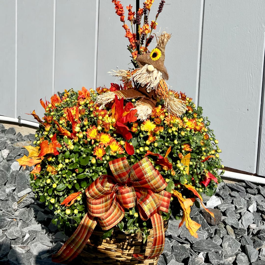 Fall flower basket with orange blooms, a scarecrow topper, and a plaid bow