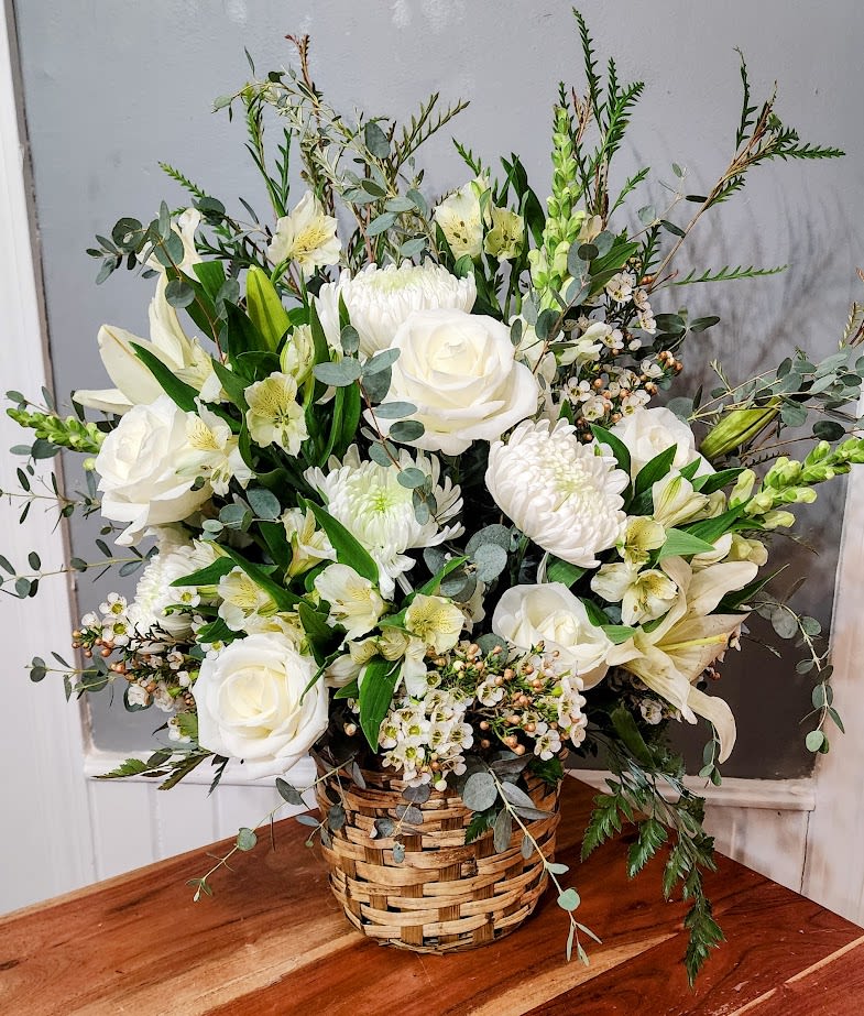 White floral arrangement in a woven basket with roses and lilies