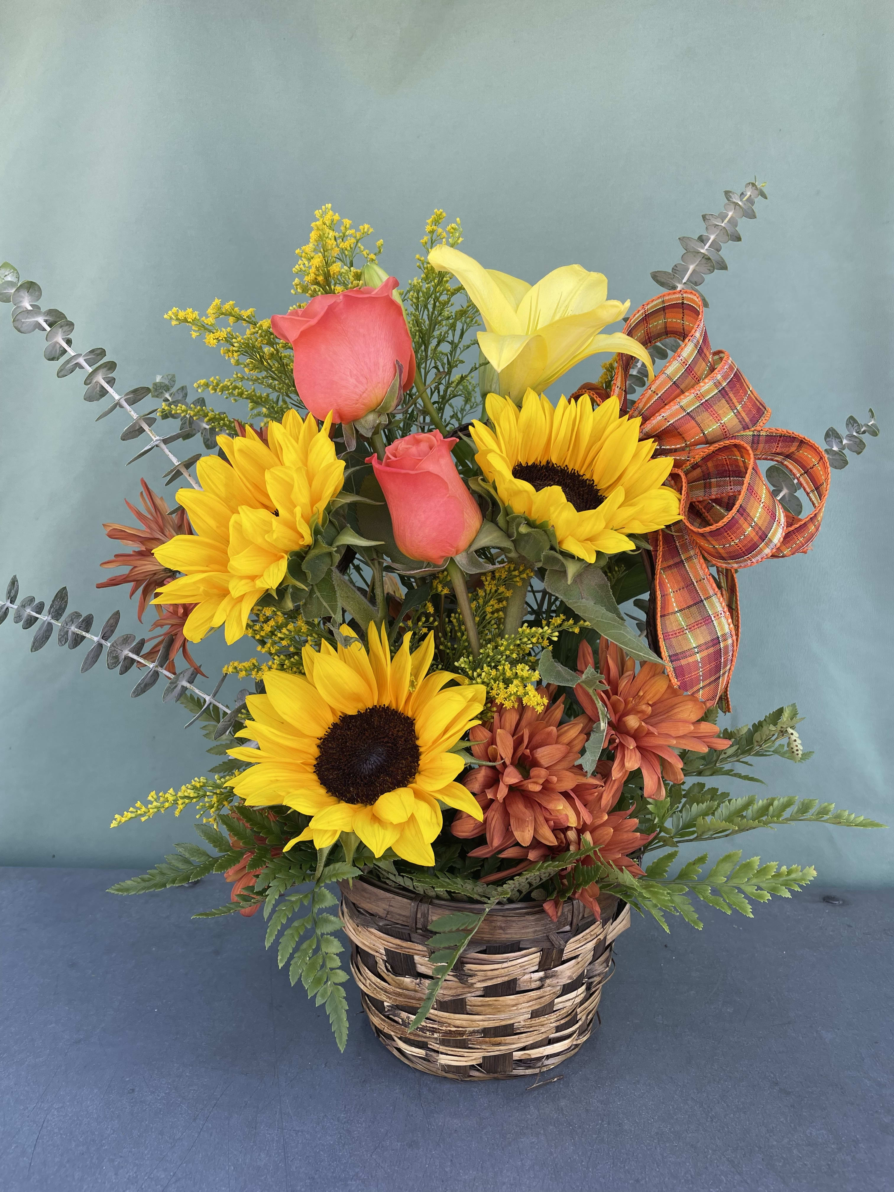 Basket arrangement with sunflowers, pink roses, and a yellow lily with plaid ribbon