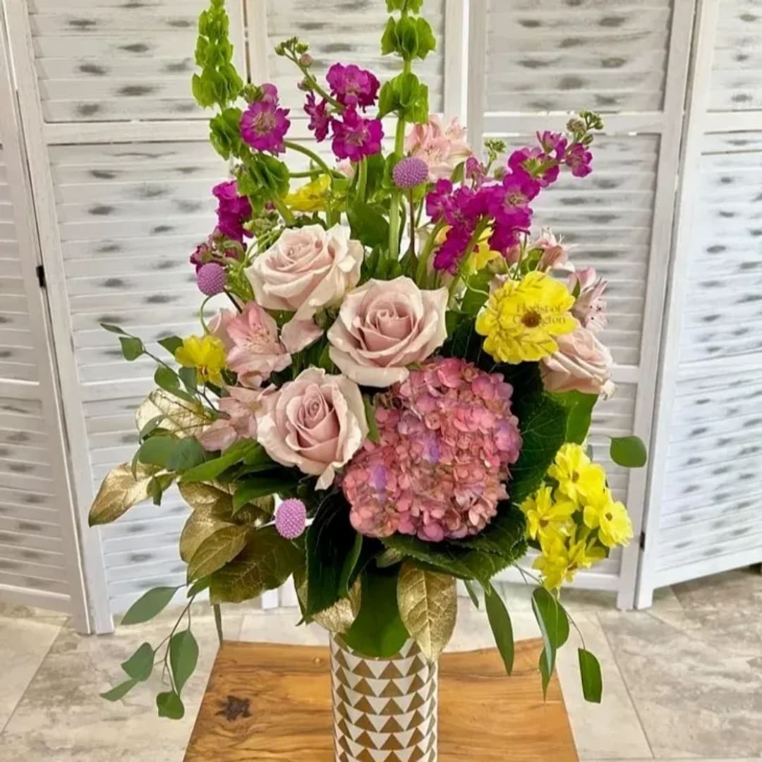 Mixed bouquet of pale pink roses, yellow blooms, and magenta flowers in a patterned vase