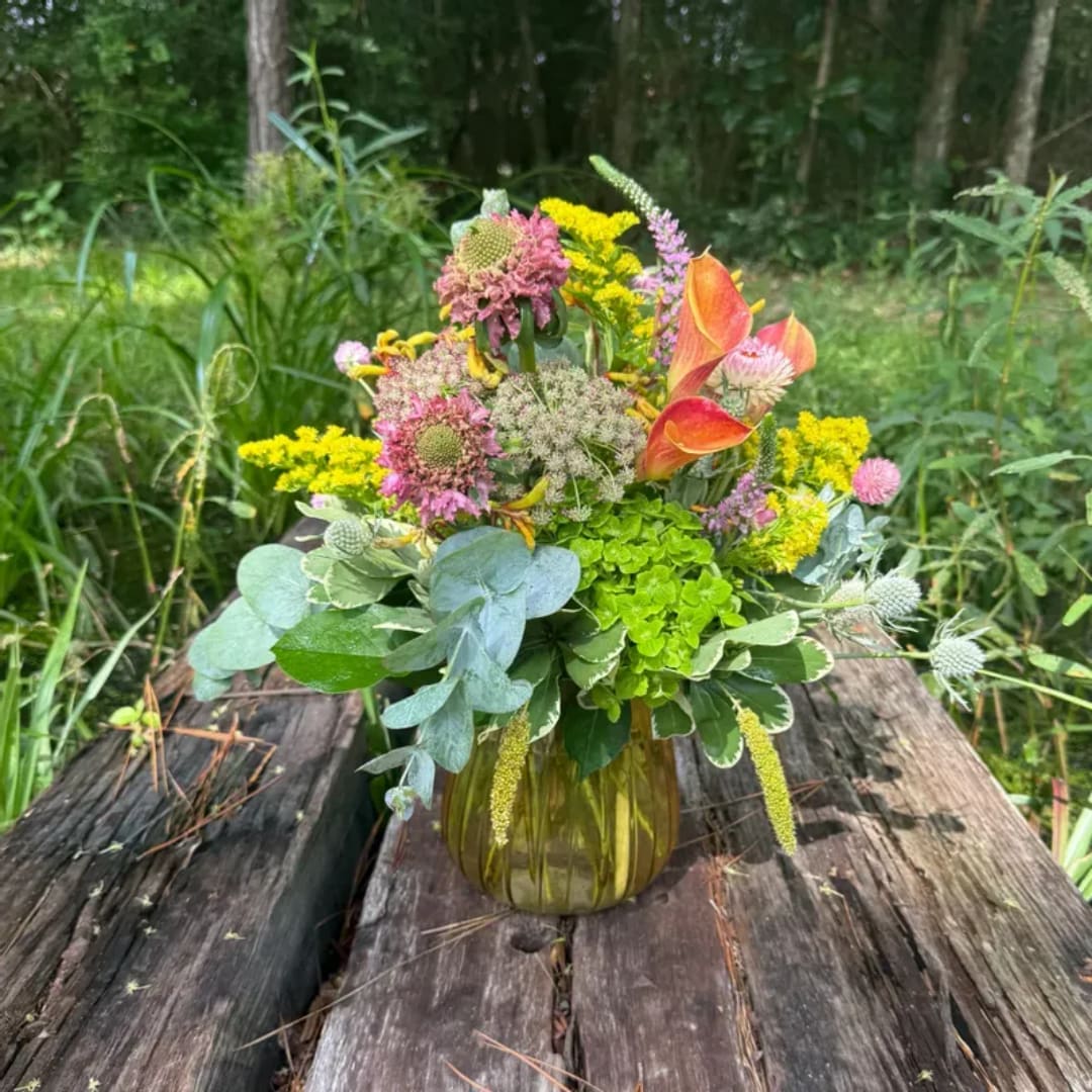Mixed bouquet in an amber glass vase with orange calla lilies and pink and yellow blooms