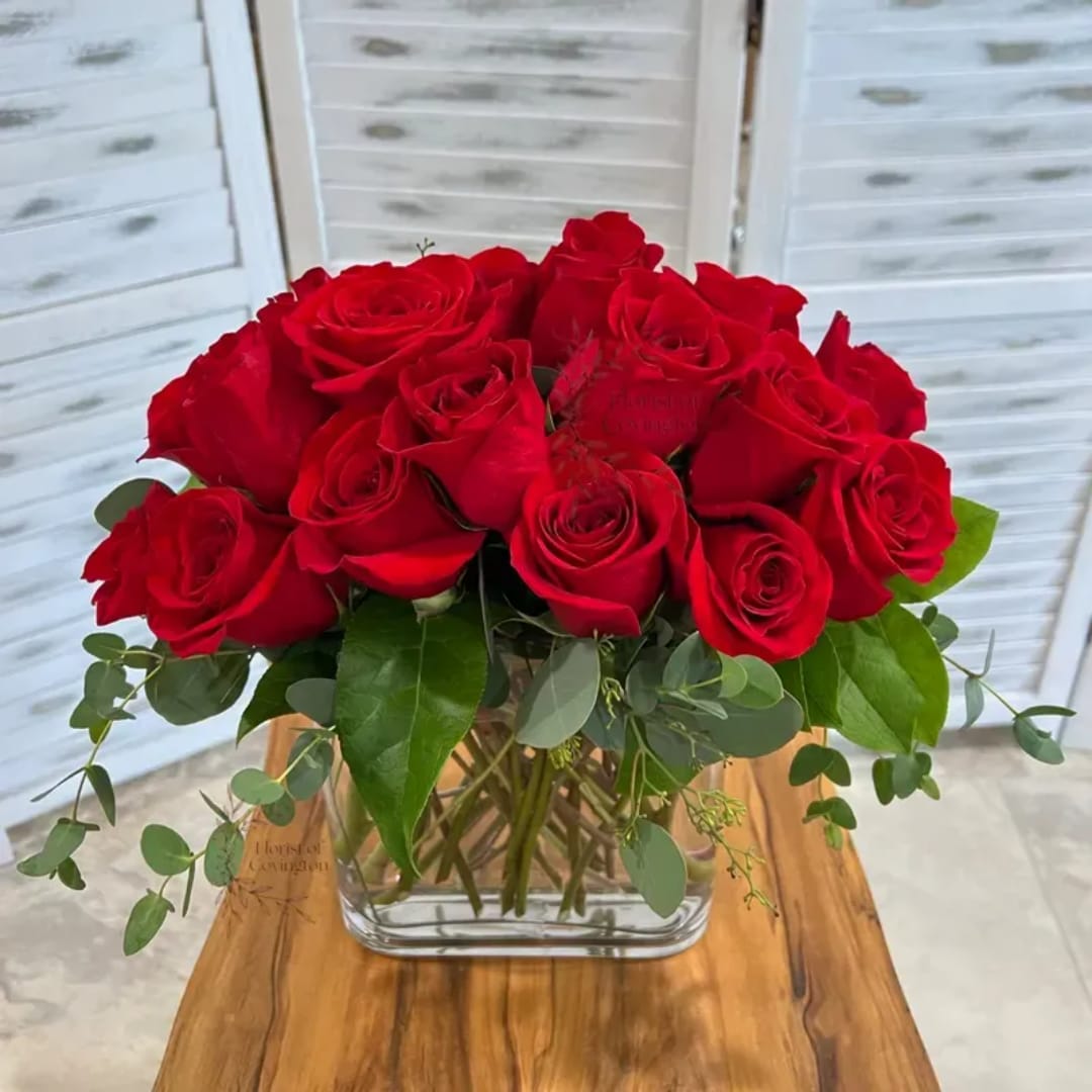 Red roses arranged in a clear glass vase with greenery