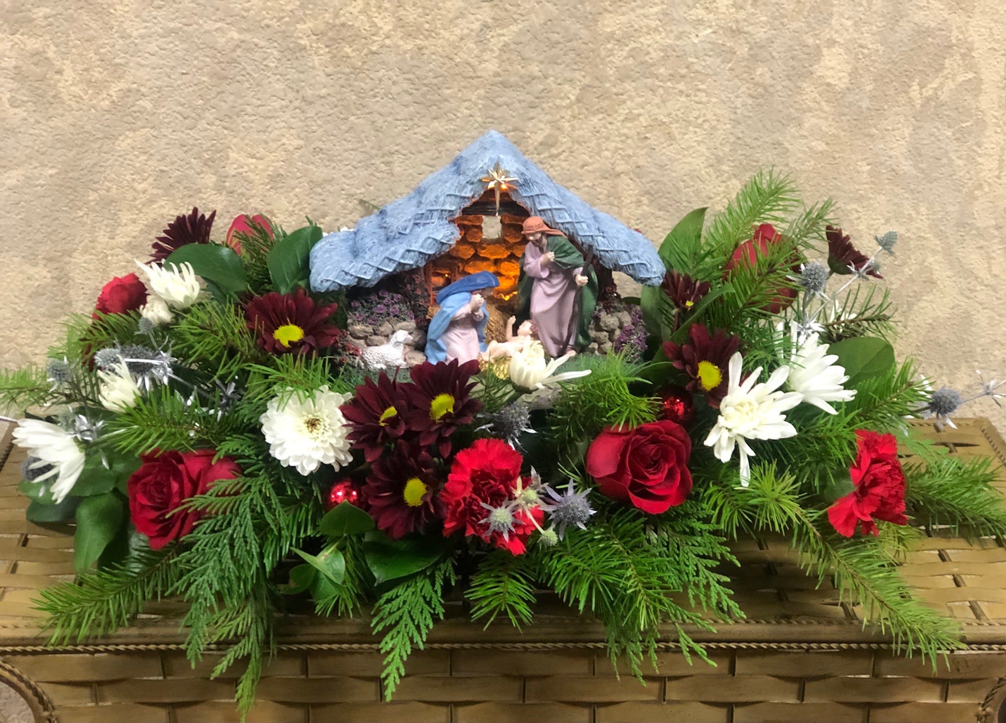 Nativity Scene Centerpiece - Type Of Flowers: Red Roses, Red Carnations, Red Daisies, White Cushions Moms,‌ ‌Pine‌ ‌greens‌, and a nativity centerpiece.‌ ‌ Availability:‌ ‌All‌ ‌year‌ ‌round‌ ‌ Substitute‌ ‌Available:‌ ‌Yes‌ ‌ Design‌ ‌View:‌ ‌All‌ ‌Facing‌ ‌View‌ ‌ 