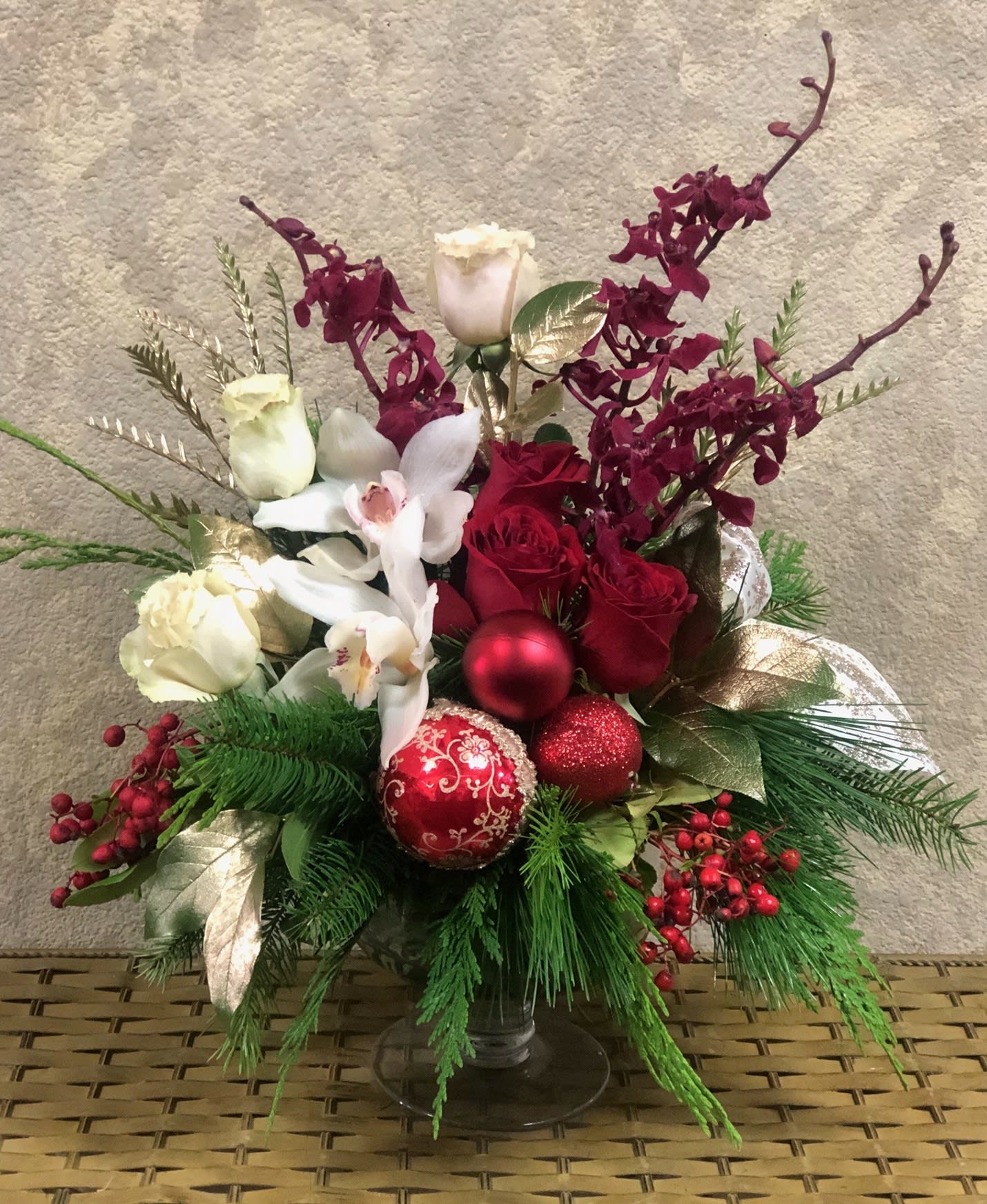 Noel - Type of Flowers: White Cymbidium Orchids, White Roses, Red Roses, Burgendy Orchids, Pine greens, and berries with red ornaments and ribbon in a short vase. Availability: All year round Substitute Available: Yes Design View: All Facing View Photo shown: Regular 