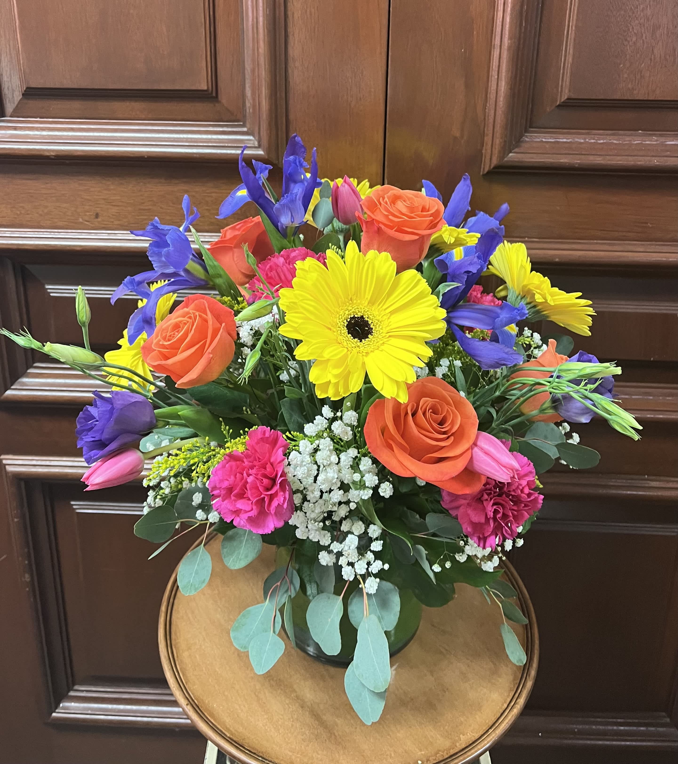 Bright mixed bouquet with yellow gerbera daisies, orange roses, and purple irises in a vase