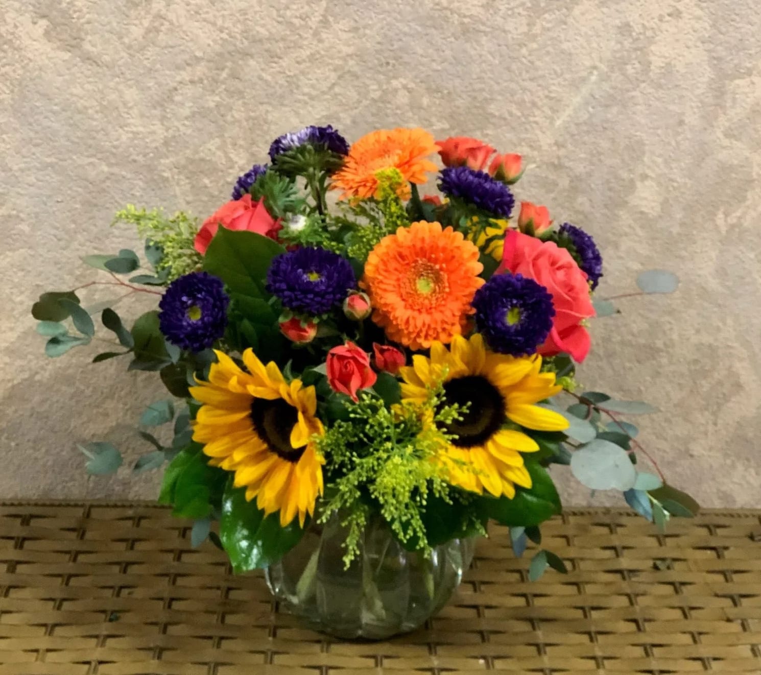 Take It Easy - Type of Flowers: Sunflowers, Coral Roses, Orange Spray Roses, Orange Gerbera Daisies, Purple Chrysanthemums, and more in a short vase. Availability: All year round Substitute Available: Yes Design View: All Facing View Photo shown: Regular 