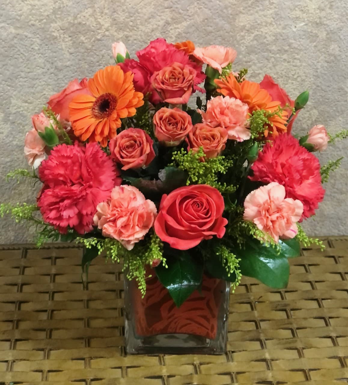 Sunrise - Type of Flowers: Orange Gerberas, Orange Roses, Orange Spray Roses, Pink Mini, and Regular Carnations in a short vase with an orange wrap. Availability: All year round Substitute Available: Yes Design View: All Facing View Photo shown: Regular