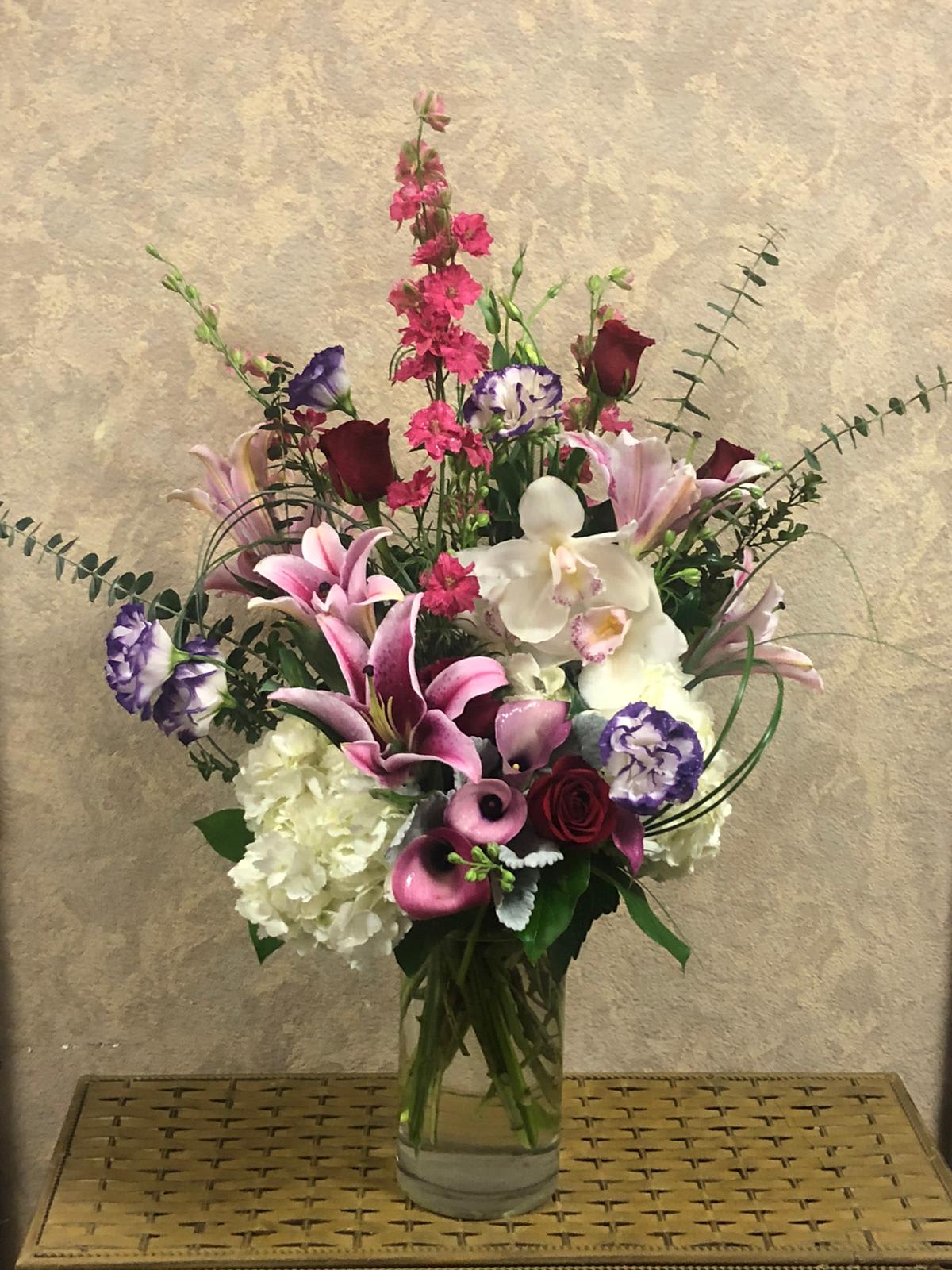 Staycation - Type of Flowers: Purple Lisianthus, Stargazers, Cymbidium Orchids, White Hydrangeas, Pink Larkspur, Red Roses, Calla Lilies, and greens in a tall vase. Availability: All year round Substitute Available: Yes Design View: All Facing View Photo shown: Regular