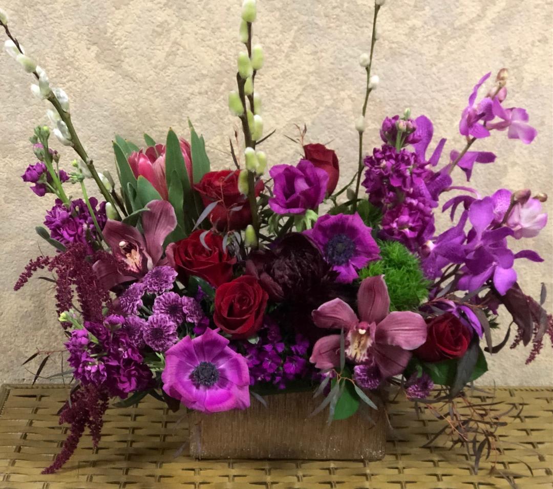 How Deep is Your Love - Type of Flowers: Give your sweetheart this red, Fushion, Tropical piece with Burgundy Peonies (seasonal), Cymbidium Orchids, Orchids, Pink Stock, Fushion Anemones (seasonal), Protea, Red Roses, Sweet William, Dianthus barbatus, Amaranthus, Button Mums in a silver rectangular vase. Availability: Seasonal Anemones- November-March and end of summer (August) Peonies: November-mid-August Substitute Available: Yes Design View: Symmetric Front Facing View Photo shown: Regular