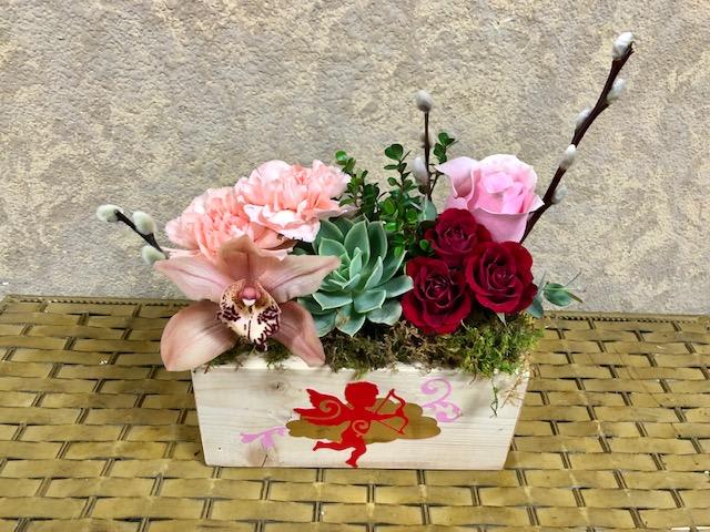Cupid's Arrow with Succulent - Type of Flowers: Red Spray Roses, Pink Carnations, Pink Cymbidium Orchid, Pink Rose, Green Succulent, and Pussy Willow in a handmade, reusable wooden box. Availability: All year round Substitute Available: Yes Design View: Symmetric Front Facing View Photo shown: Regular 