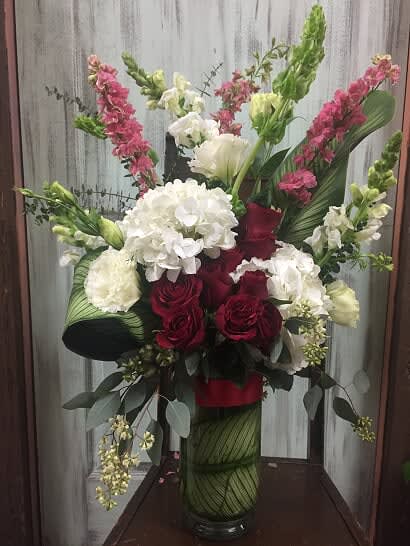 Your Love Changes Everything - Type of Flowers: Red Roses, White Hydrangeas, White Lisianthus, White Snap Dragon, Pink Larkspur, Bells of Ireland, Leaf, and Greens in a tall clear vase wrapped with leaf wrap inside and red ribbon. Availability: All year round. Substitute Availability: Yes