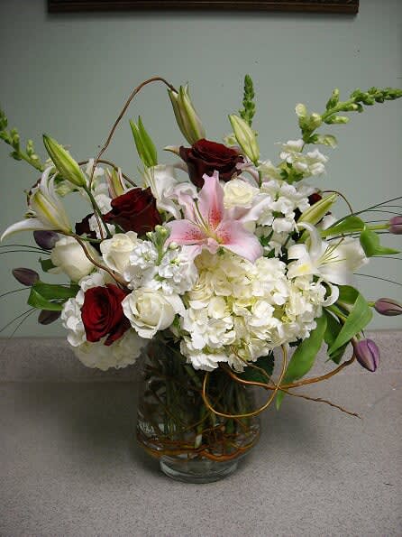 You're Divine - Recipe: White Snapdragons, Pink Stargazers Lilies, White Hydrangeas, Red Roses, Purple Tulips, Curly Willow in a clear cylinder vase. Seasonal: All year round Orientation: Front Facing View Photo shown: Standard 