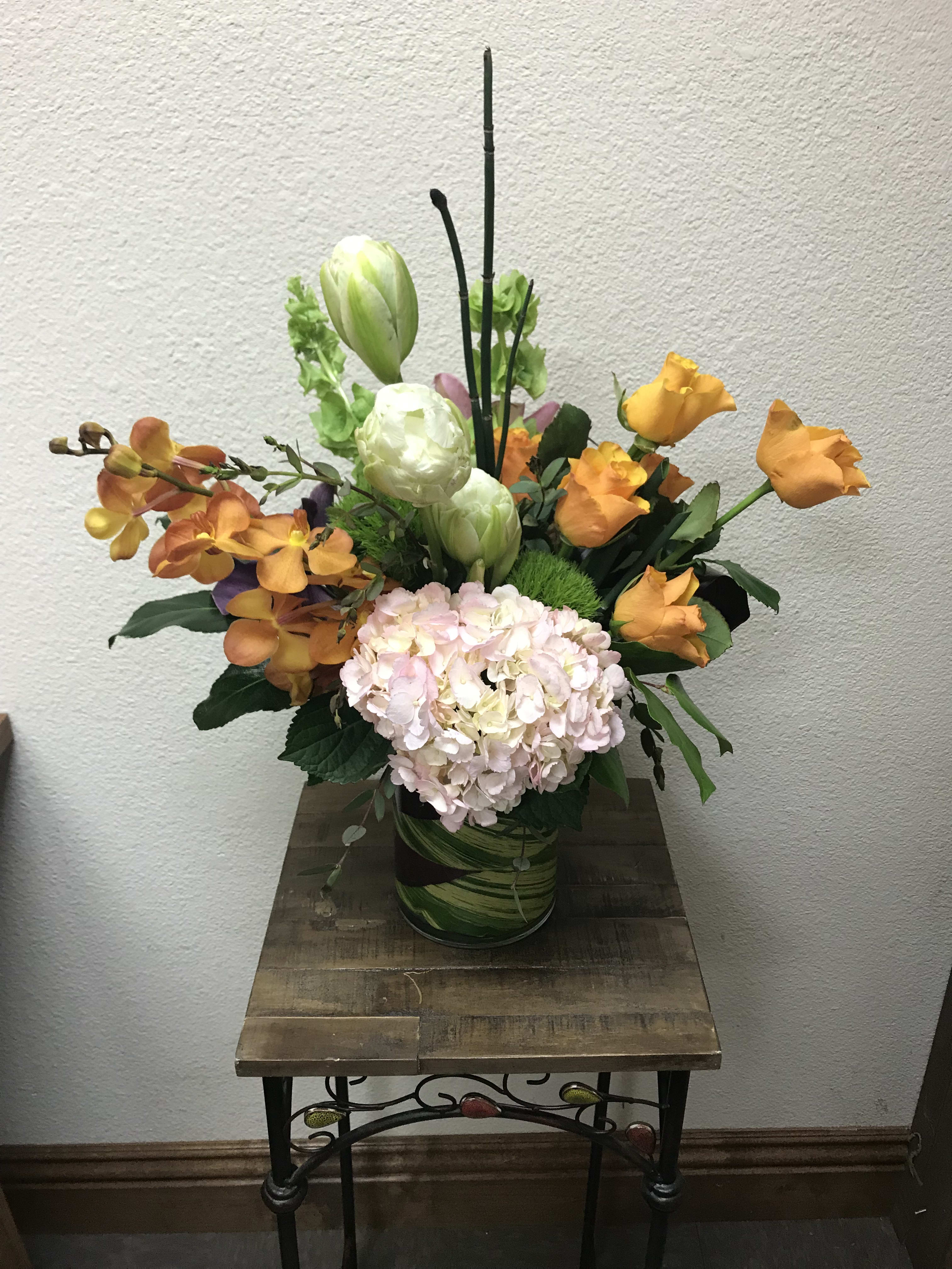 Maui Sunrise - Type of Flowers: Roses, Orchids, Parrot Tulips (Seasonal) Hydrangea, Lilies, Bells of Ireland, and more with a leaf wrap in a tall vase. Availability: Winter Substitute Available: Yes Design View: All-Sided Facing View Photo shown: Standard 