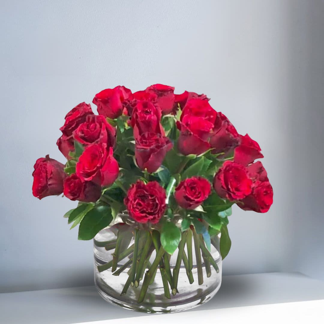 Compact arrangement of red roses in a clear glass cylinder vase