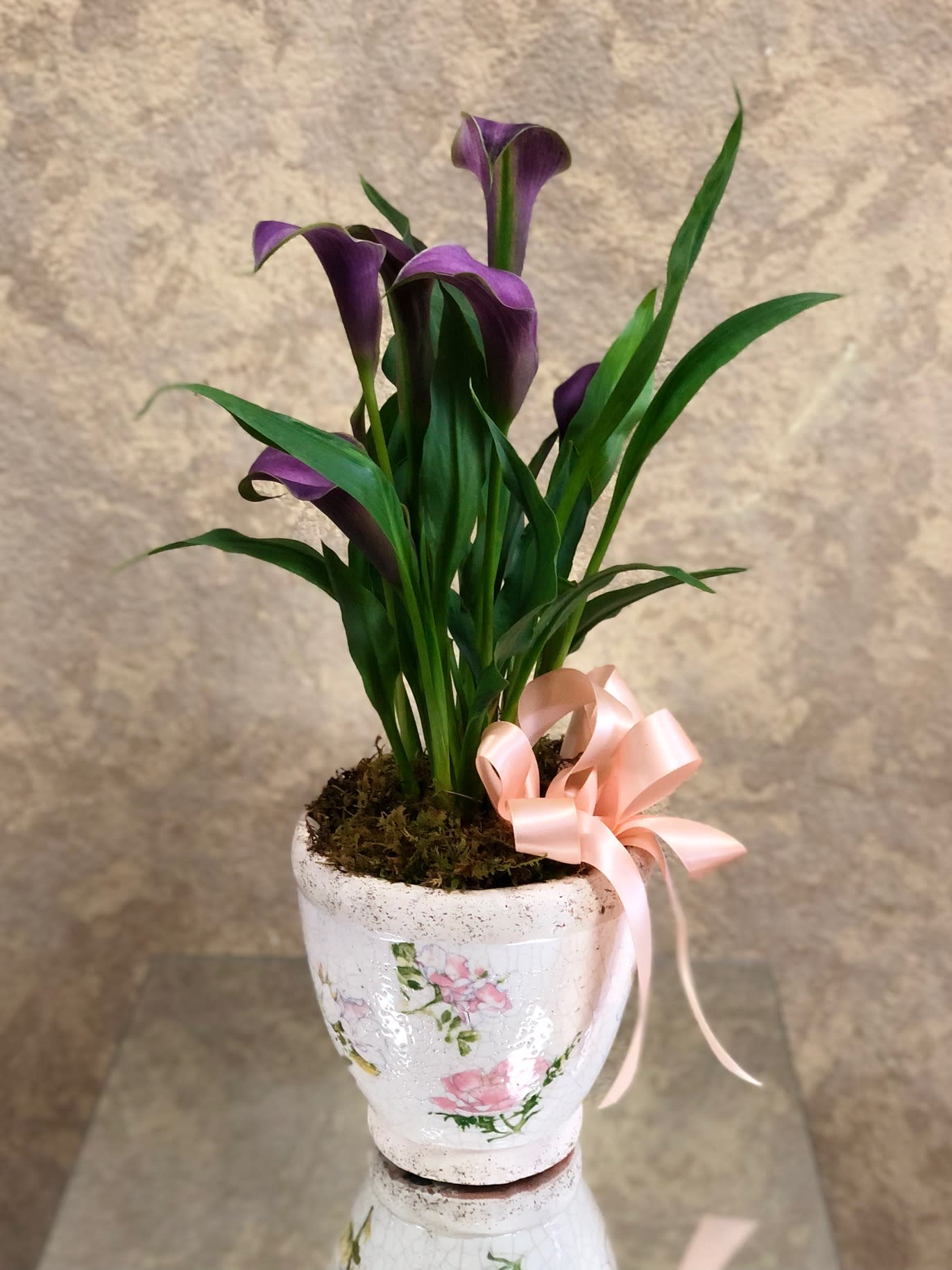 Purple calla lilies in a white floral pot with a pink ribbon