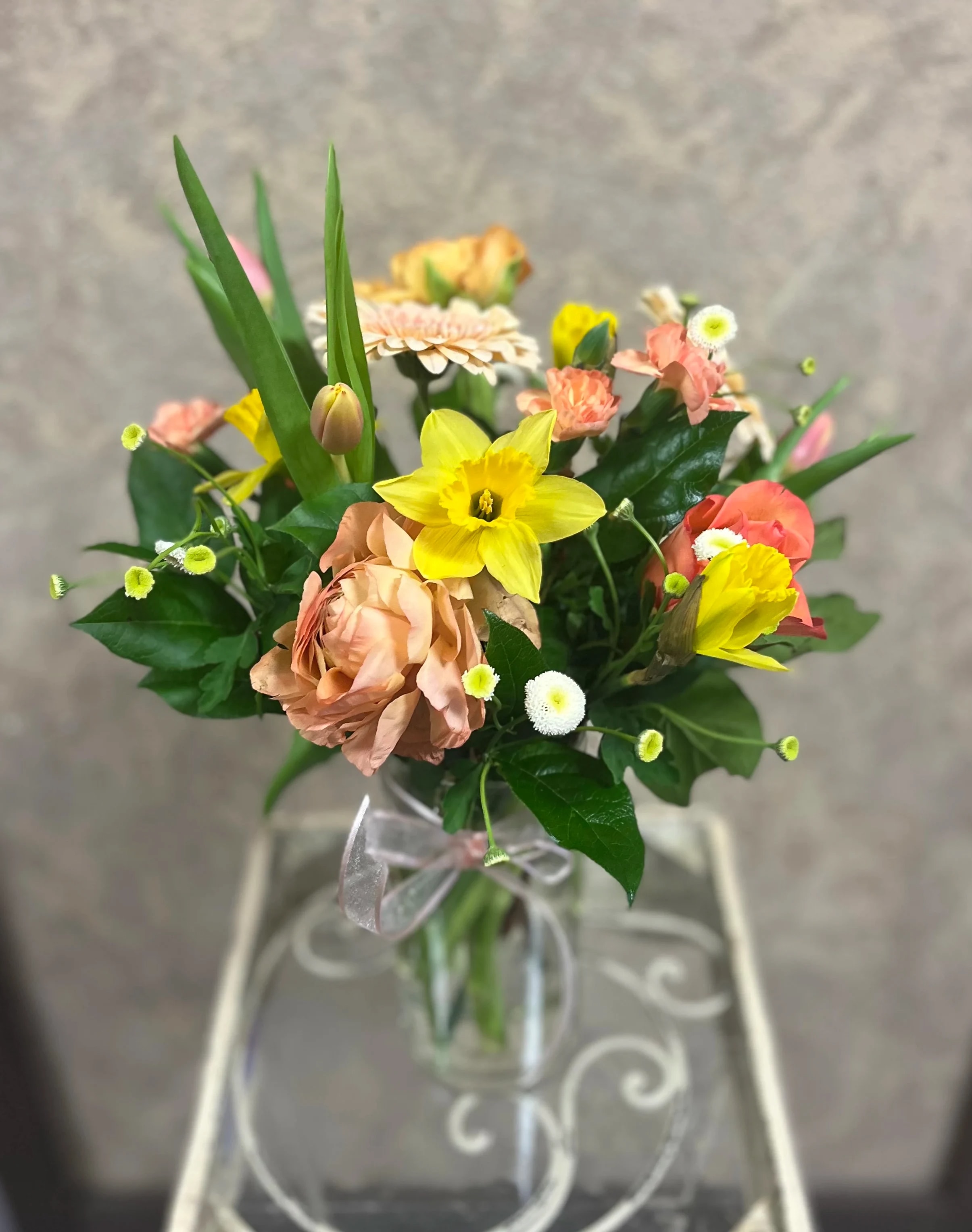 Mixed bouquet with yellow daffodils, peach roses, and small white daisies in a glass vase
