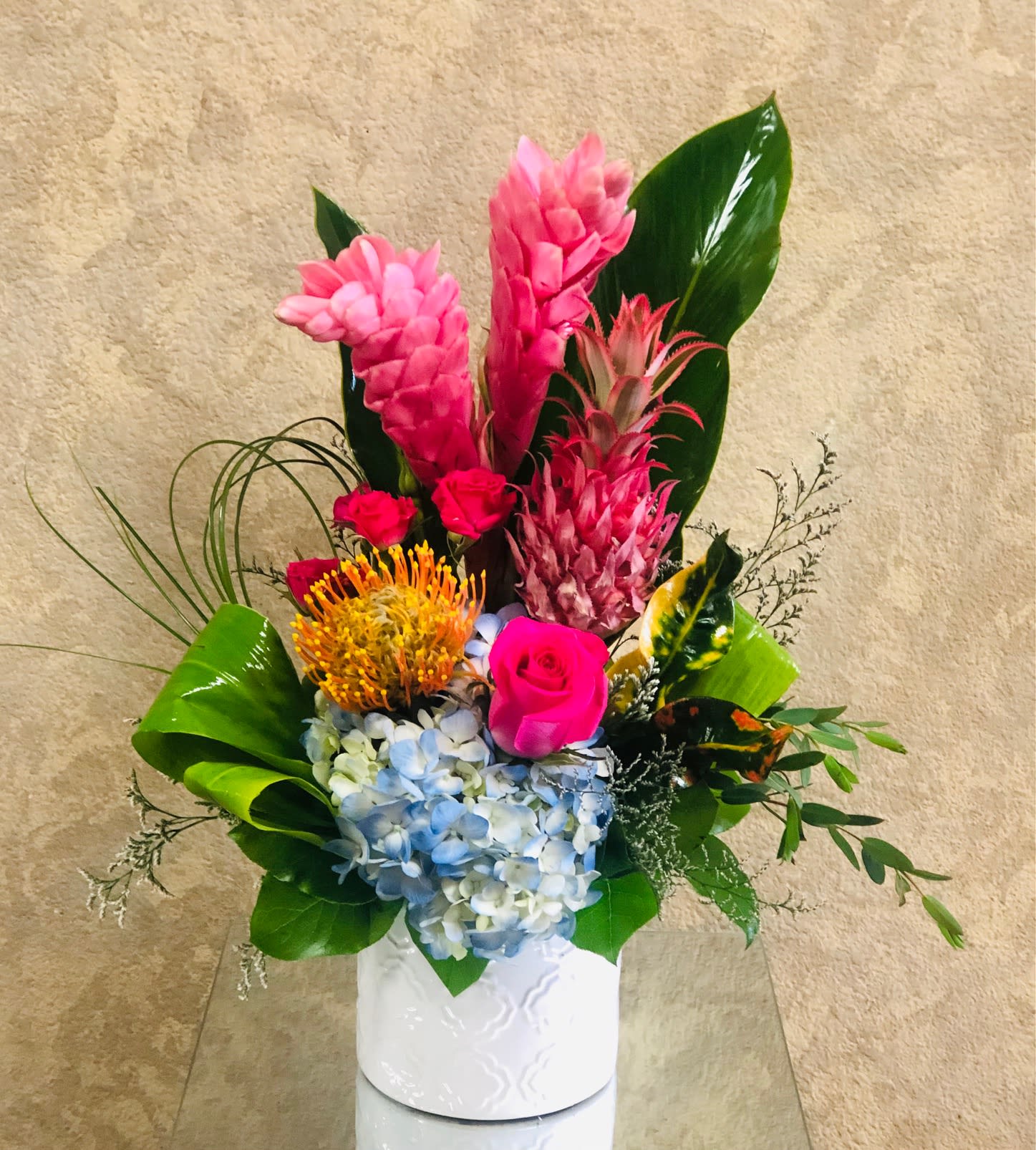 Wear a Crown like a Pineapple - SPECIAL THIS WEEK ONLY!! Lovely arrangement with a mini pineapple, pink ginger, cushion protea, hot pink rose, and hot pink mini roses in a white ceramic vase.