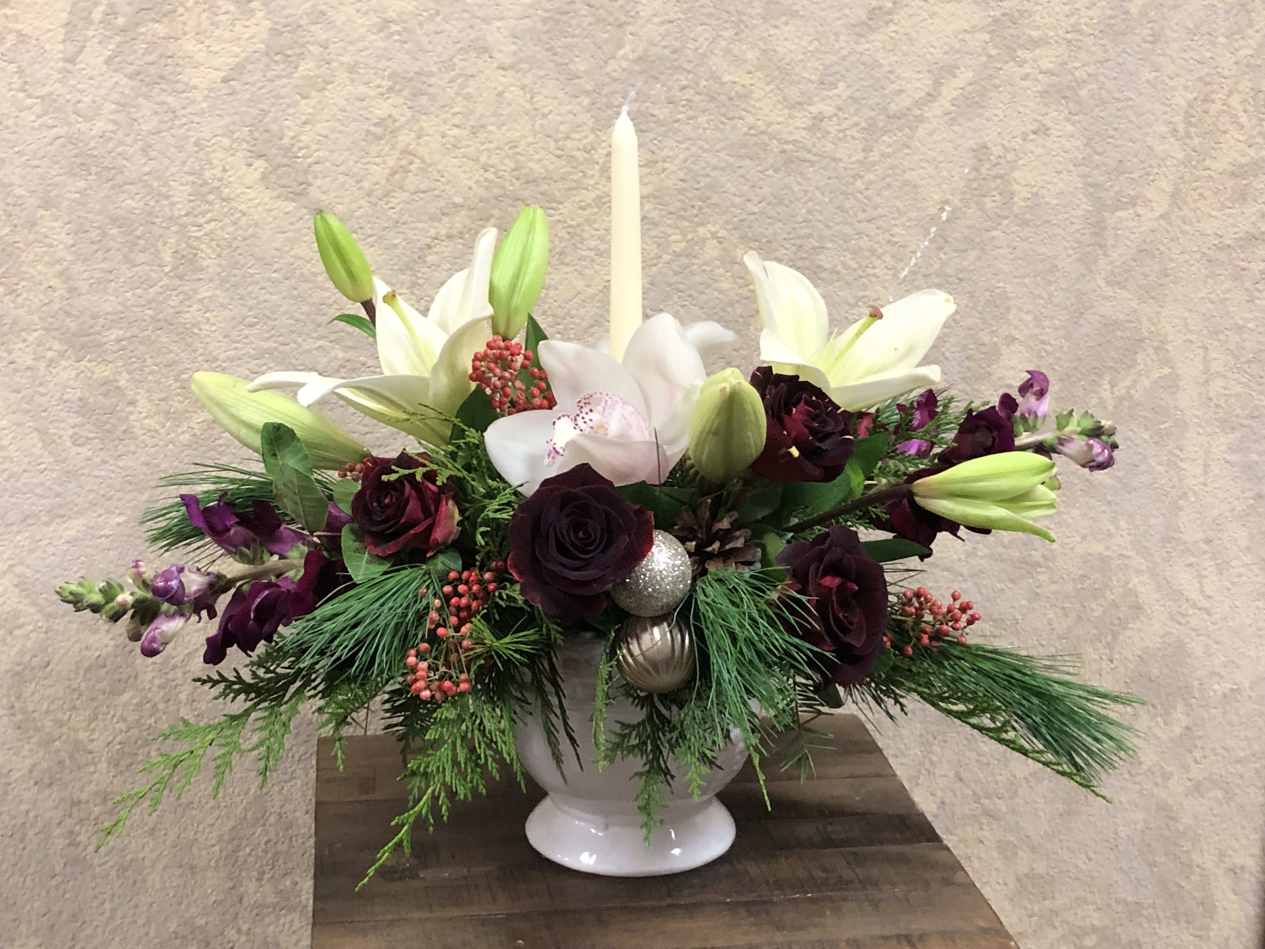 Seasons Greetings Centerpiece - Christmas centerpiece with white orchids, white lillies, red roses purple cymbidium orchids, pine greens with silver ornaments and candle in a white plaster (deluxe) or silver, glass porcelain (premium). Pictures shown are regular and premium value.