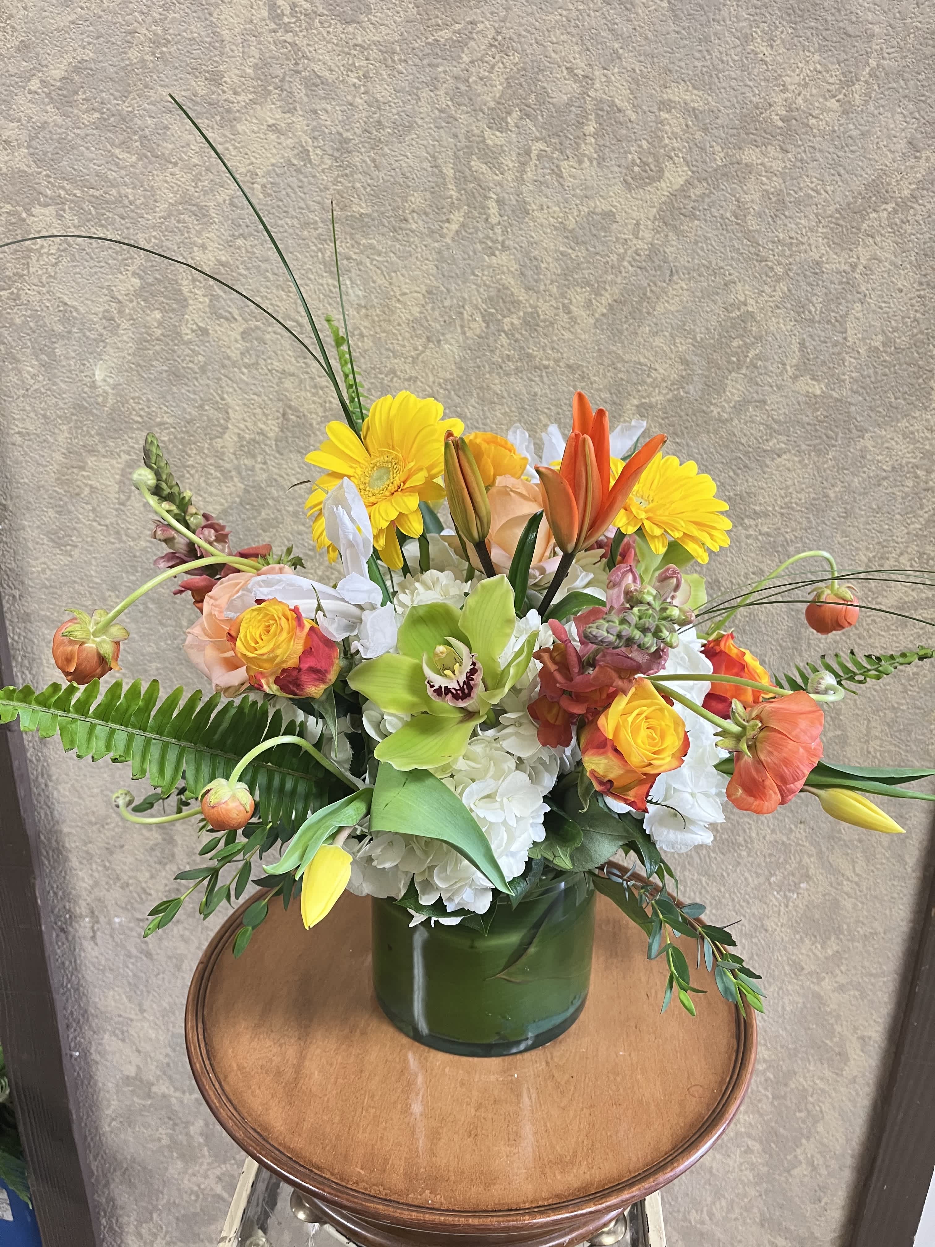 Hello Sunshine - This bright design is cheerful and fun with seasonal flowers popping out all around! Recipe: White Hydrangaes, Pink Snapdragons, Green Cymbidium Orchids, Orange Asiatic Lilies, Yellow Roses, Orange Ranculus (seasonal), Yellow Gerbera Daisies, White Iris, Yellow Tulips, Bear Grass and Fern in a clear, cylinder vase. Availability: All year round Design View: All Facing View Photo shown: Standard 