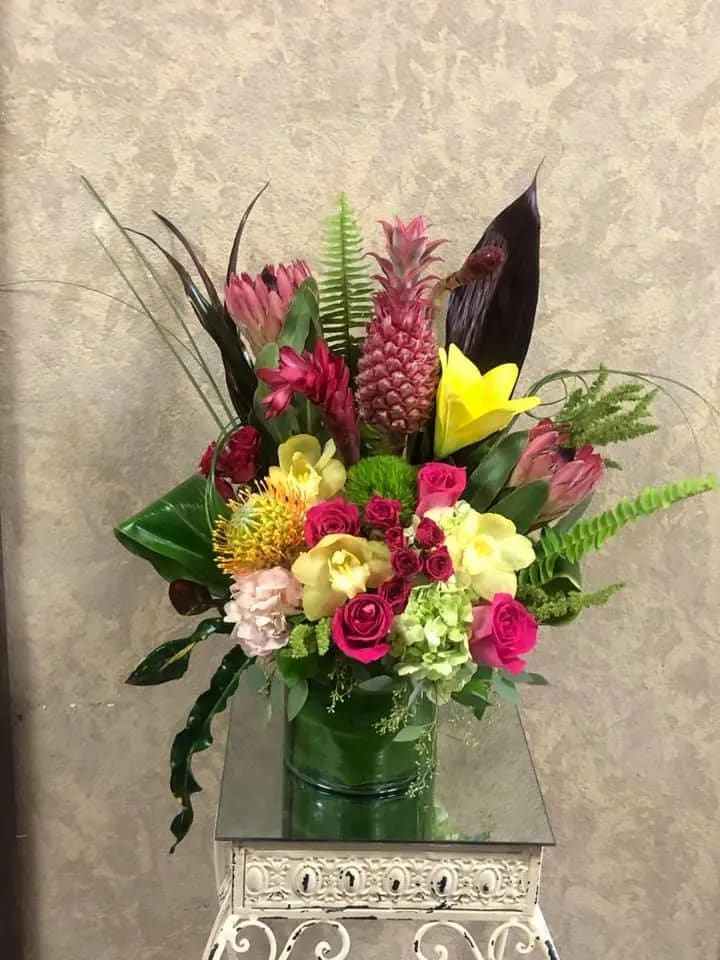 Sunny Pineapples - Fresh, Sweet, and Tropical. We're celebrating summer with our Sunny Pineapples. Great idea for Tropical, Aloha Parties! Type of Flowers: Pink Pineapple, Cymbidium Orchids, Regular Roses, Hydrangeas, Lilies, Spray Roses, Tropical greens, and more with a leaf wrapped in a short crystal vase. Availability: All year round Design View: Front Facing View Photo shown: Regular