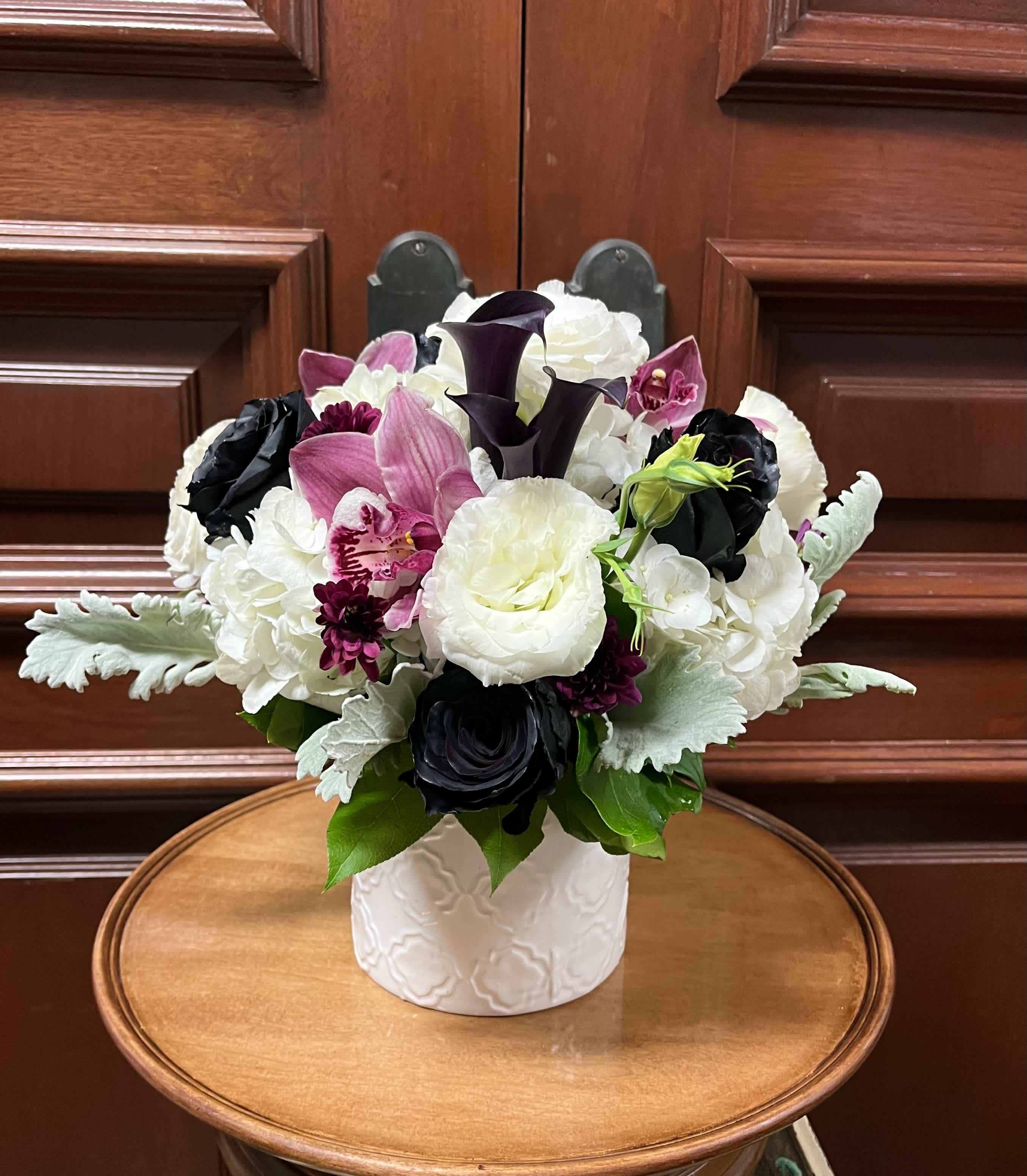 Mama You Rock! NEW - Recipe: Black Roses, Black Calla Lilies, White lisianthus, White Hydrangaes, Purple Cymbidium Orchids, Dusty Miller, and Purple Chrysanthemums in a circular, white vase. Availability: All year round Design View: Symmetric Front Facing View Photo shown: Standard