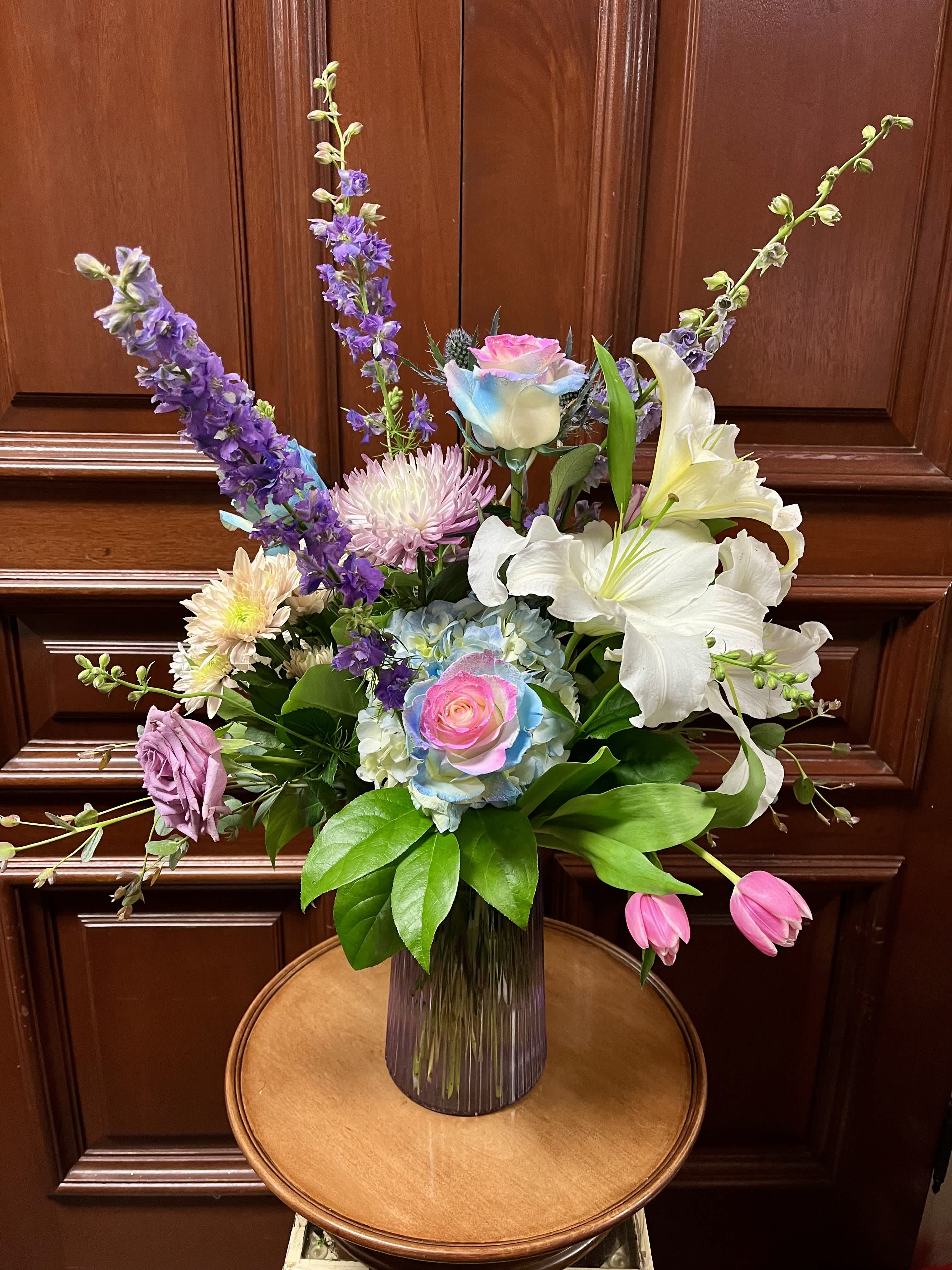 Tall mixed bouquet with lilies, roses, and purple blooms in a glass vase