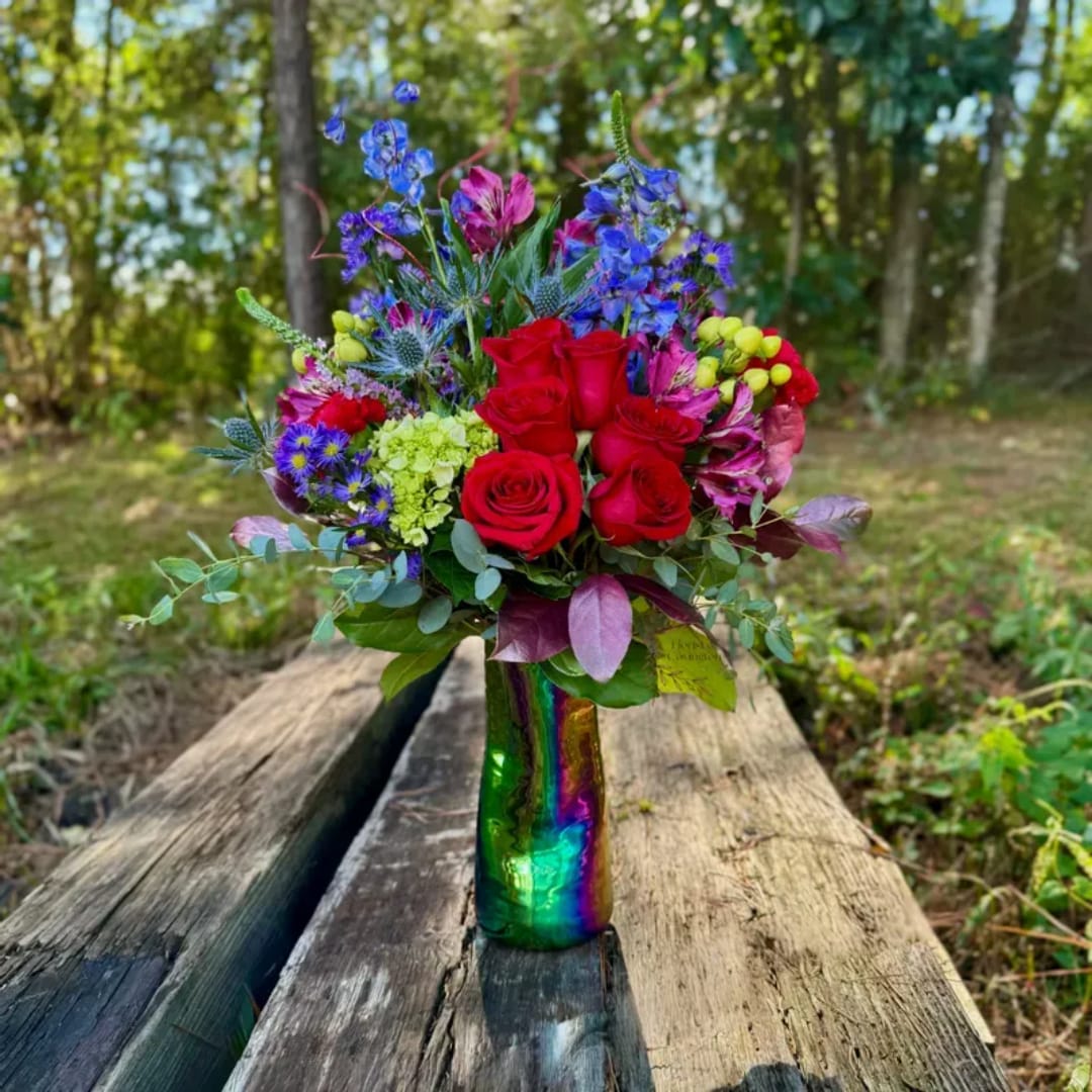 Bouquet of red roses, blue flowers, and pink blooms in a rainbow glass vase
