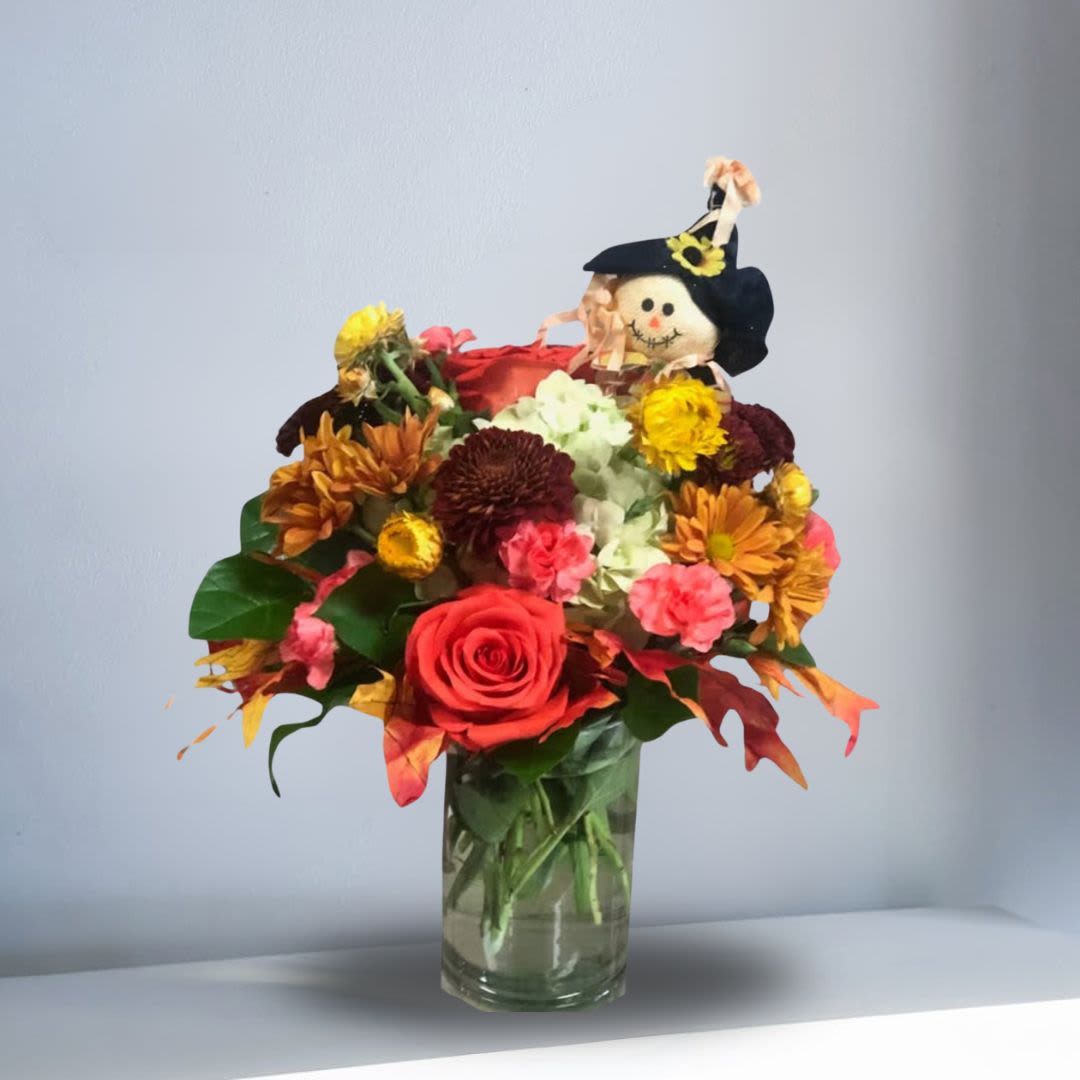 The Scarecrow SPECIAL - Arrangement for fall with silk fall leaves, hydrangea, carnations, roses, strawflowers, daisies, mums, and buttons in a short clear vase. Can be made with or without a scarecrow. Arrangement is 14in high.