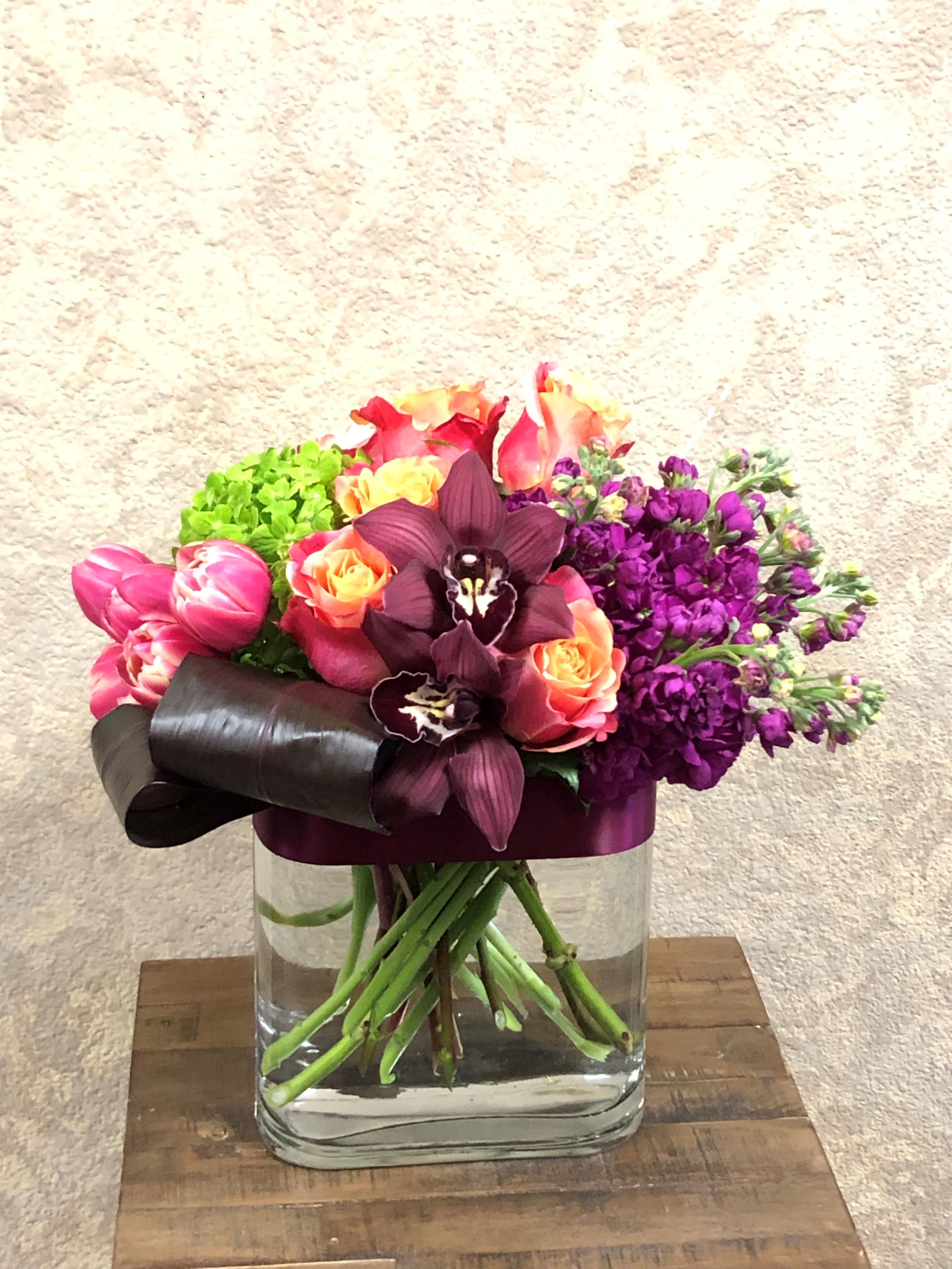 Mixed bouquet of pink, orange, purple, and green flowers in a glass vase
