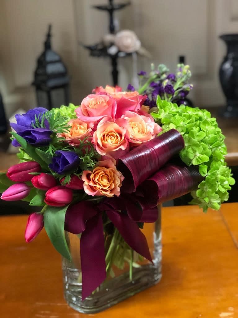 The Exquisite Bouquet  - Type of Flowers: Purple Stock, Pink Roses, Pink Tulips, Green Hydrangeas, Purple Lisianthus and more in a short clear vase with purple silk ribbon. Availability: All year round Substitute Available: Yes Photo shown: Regular