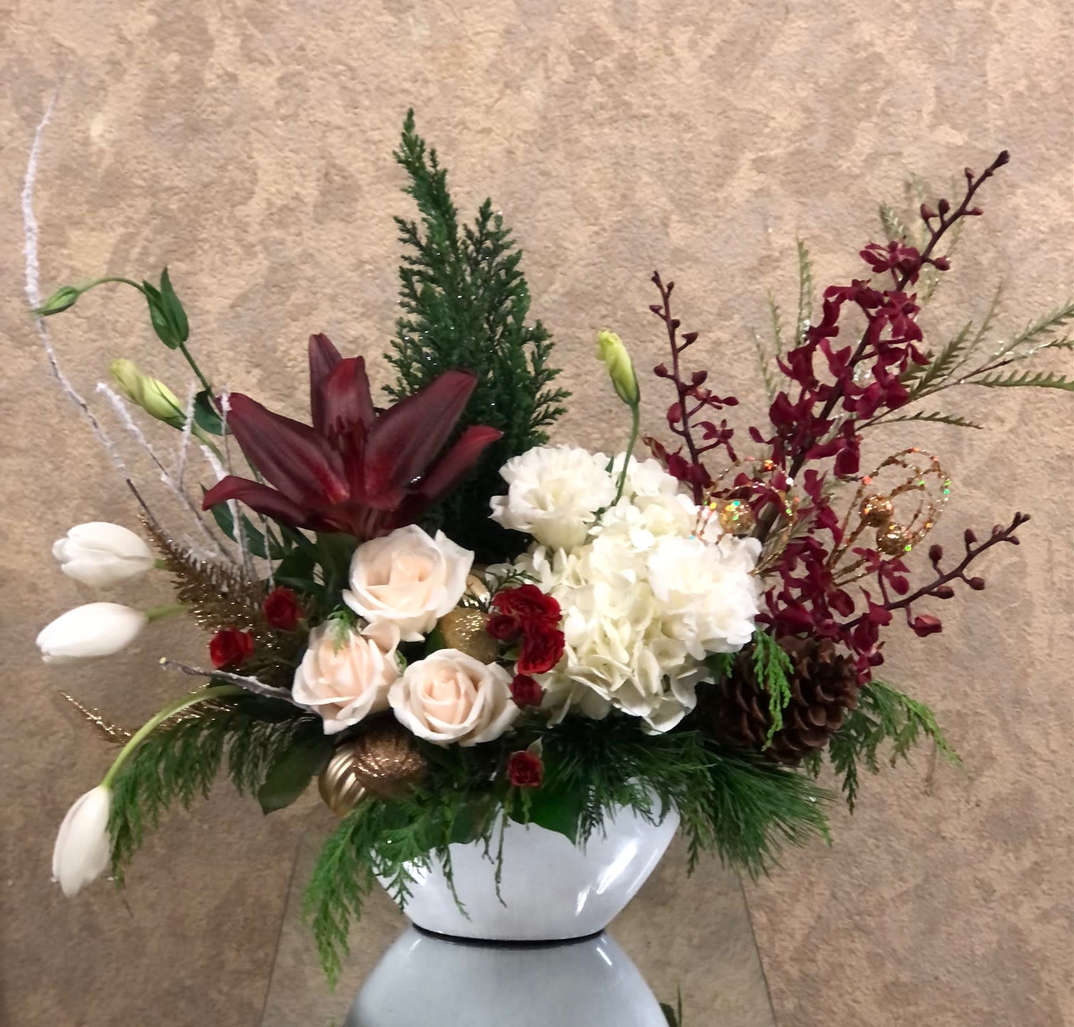 Renewal, Calm, Peace - Live pine tree, orchids, lt. pink roses, tulips, red tiger lily, lisianthus, tree ornaments, and pine greens in an oblong white vase.