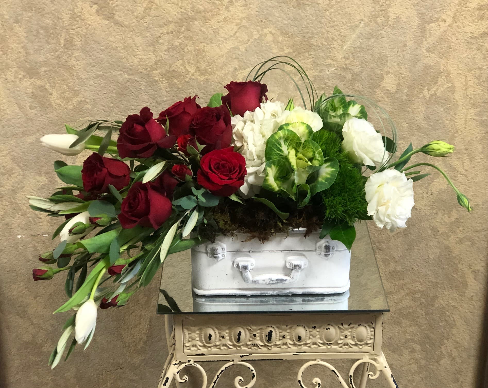 Cascading Love - Send your love this Holiday with a suitcase full of beautiful, cascade of flowers. Type of Flowers: Tulips, Spray Roses, Roses, Kale, Hydrangeas, Lisianthus, and Bear Grass in a short vase. Availability: All year round Orientation: Front Facing View Photo shown: Standards