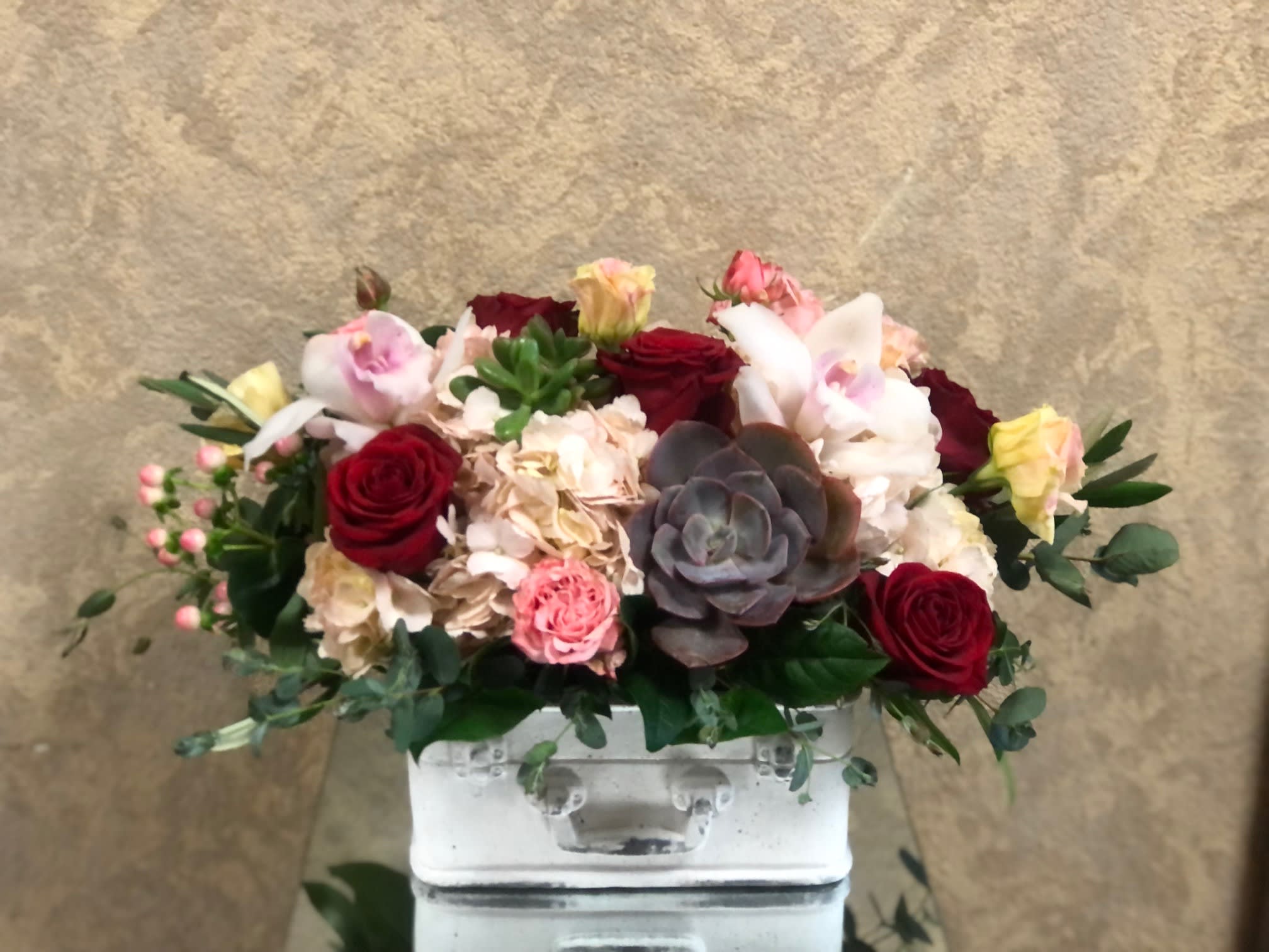Sending You My Love - Send some Valentine's love with  Type of Flowers: Roses, Hydrangea, Orchids, Spray Roses, Lisianthus, Carnations, Hypericum Berries, and Succulents in a plaster white suitcase. Availability: Suitcase limited. Substitute Available: Yes Design View: Symmetric Front Facing View Photo shown: Regular