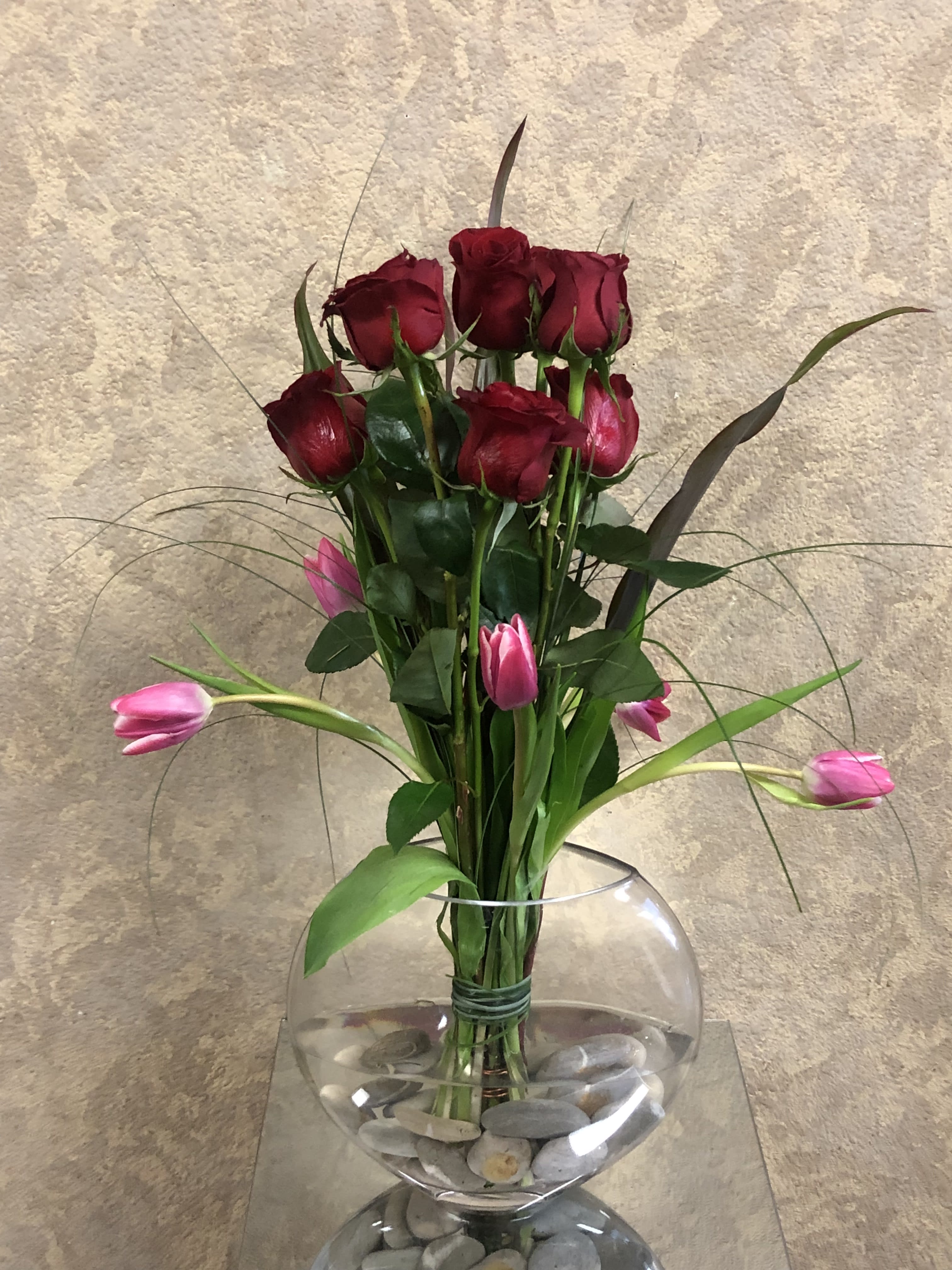 Rose Abundance  - This simple design is a combination of romance and comfort that will put the mind at ease with love. Type of Flowers: Red Roses and Pink Tulips in a circular vase with stone pebbles. Availability: All year round Substitute Available: Yes Design View: All Facing Facing View Photo shown: Regular 